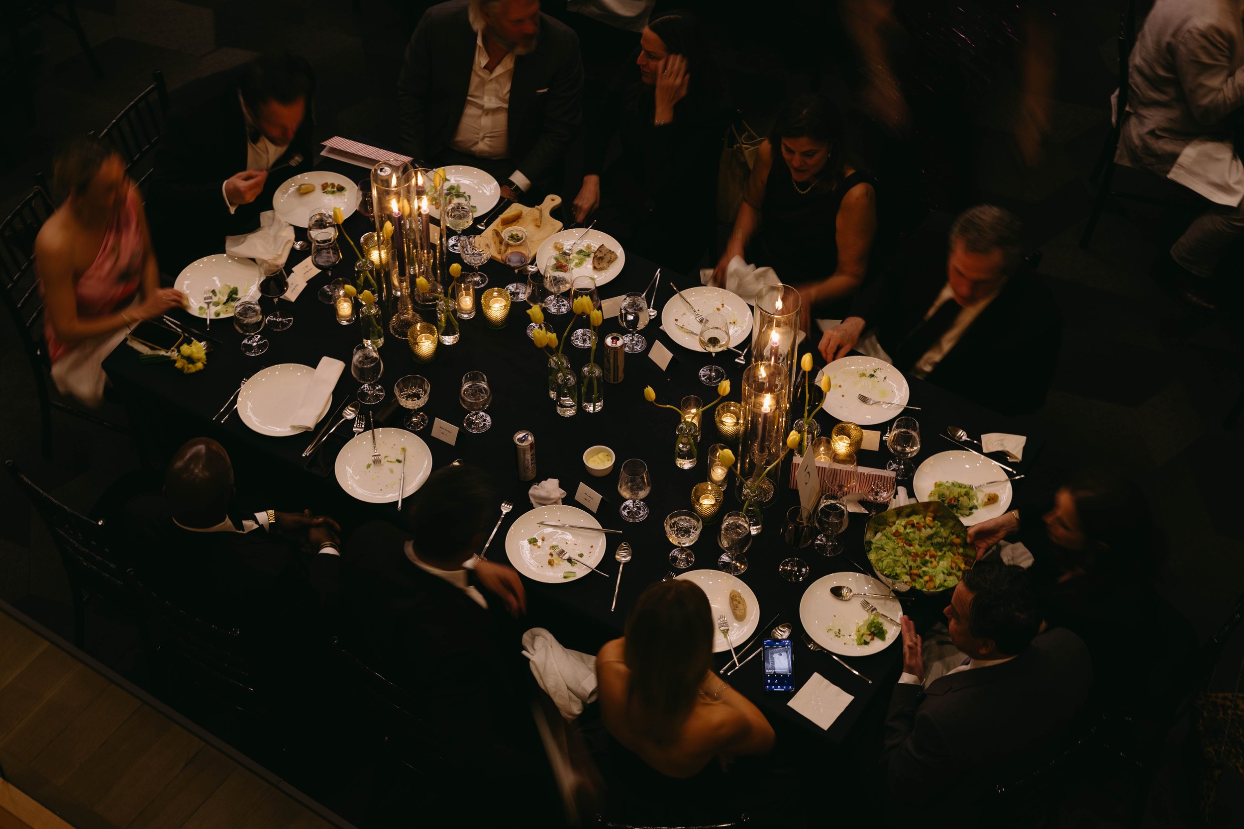 People sitting around an elegantly set dining table with plates, glassware, candles, and tulips, likely during a formal dinner event.