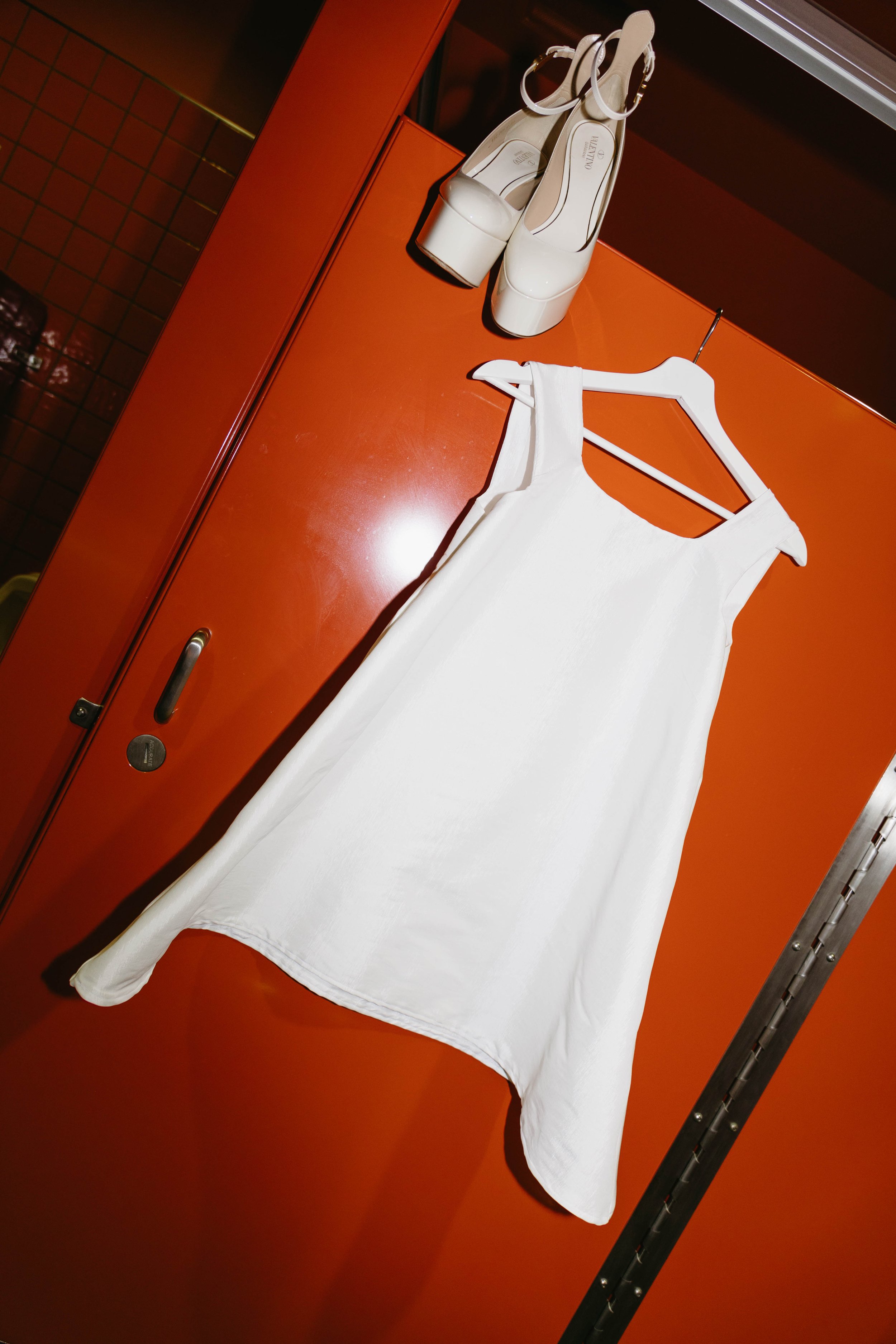 White dress hanging on red locker with white platform shoes on top.