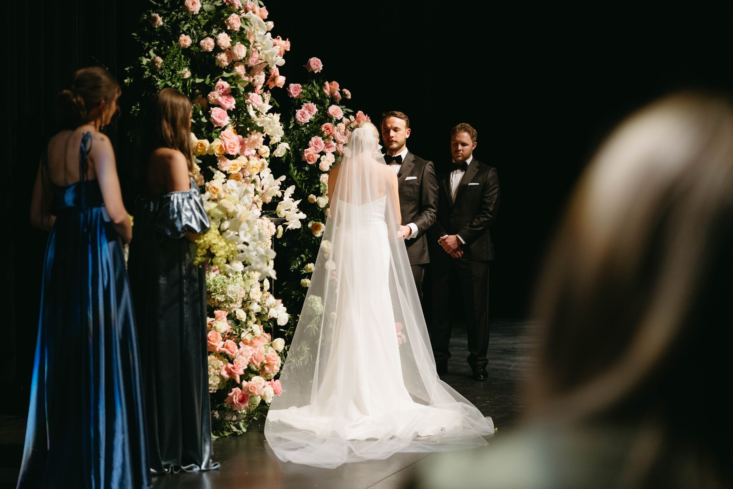 Wedding ceremony with bride, groom, bridesmaids, and floral arch.