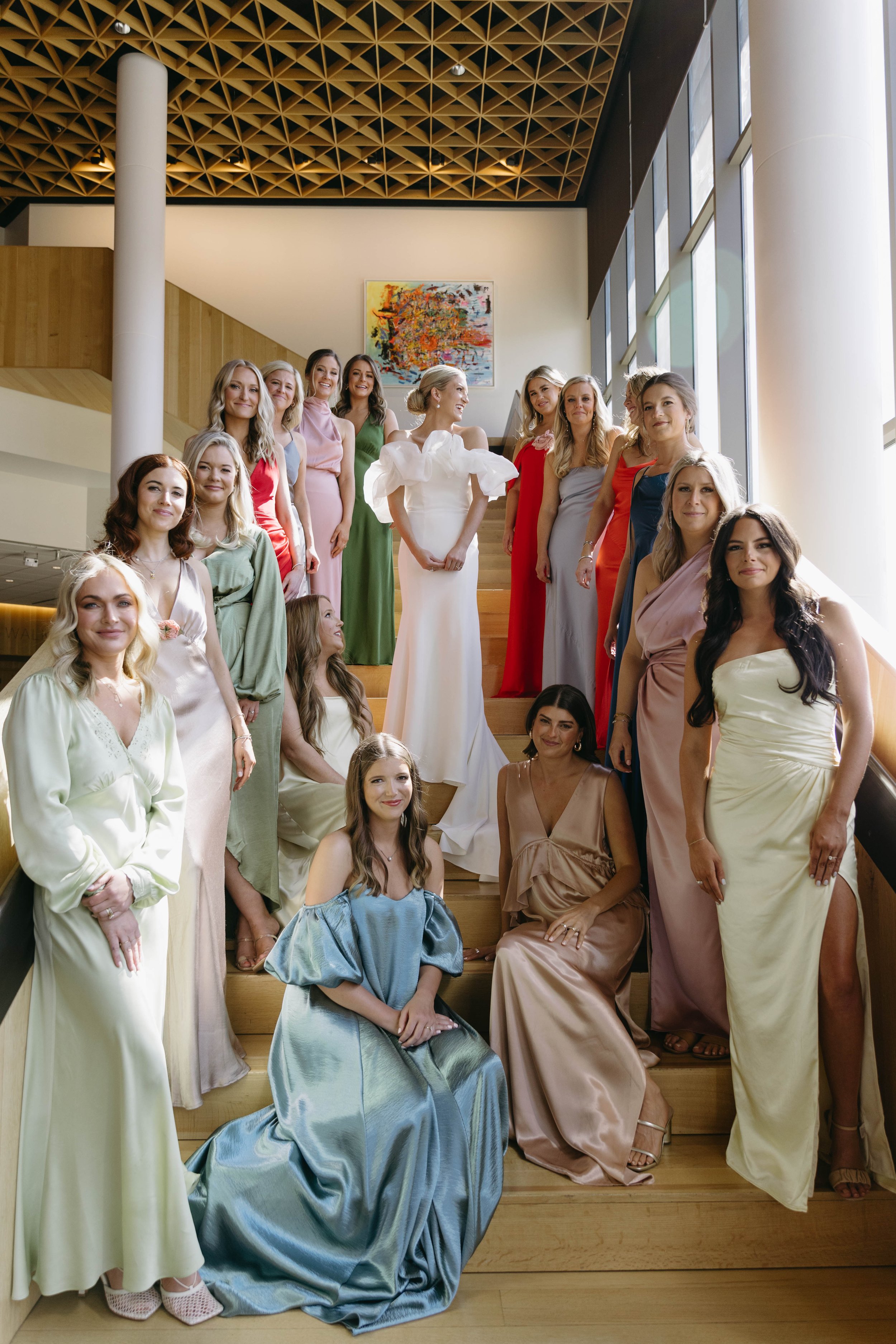 Group of women in elegant dresses posing on stairs inside a building.