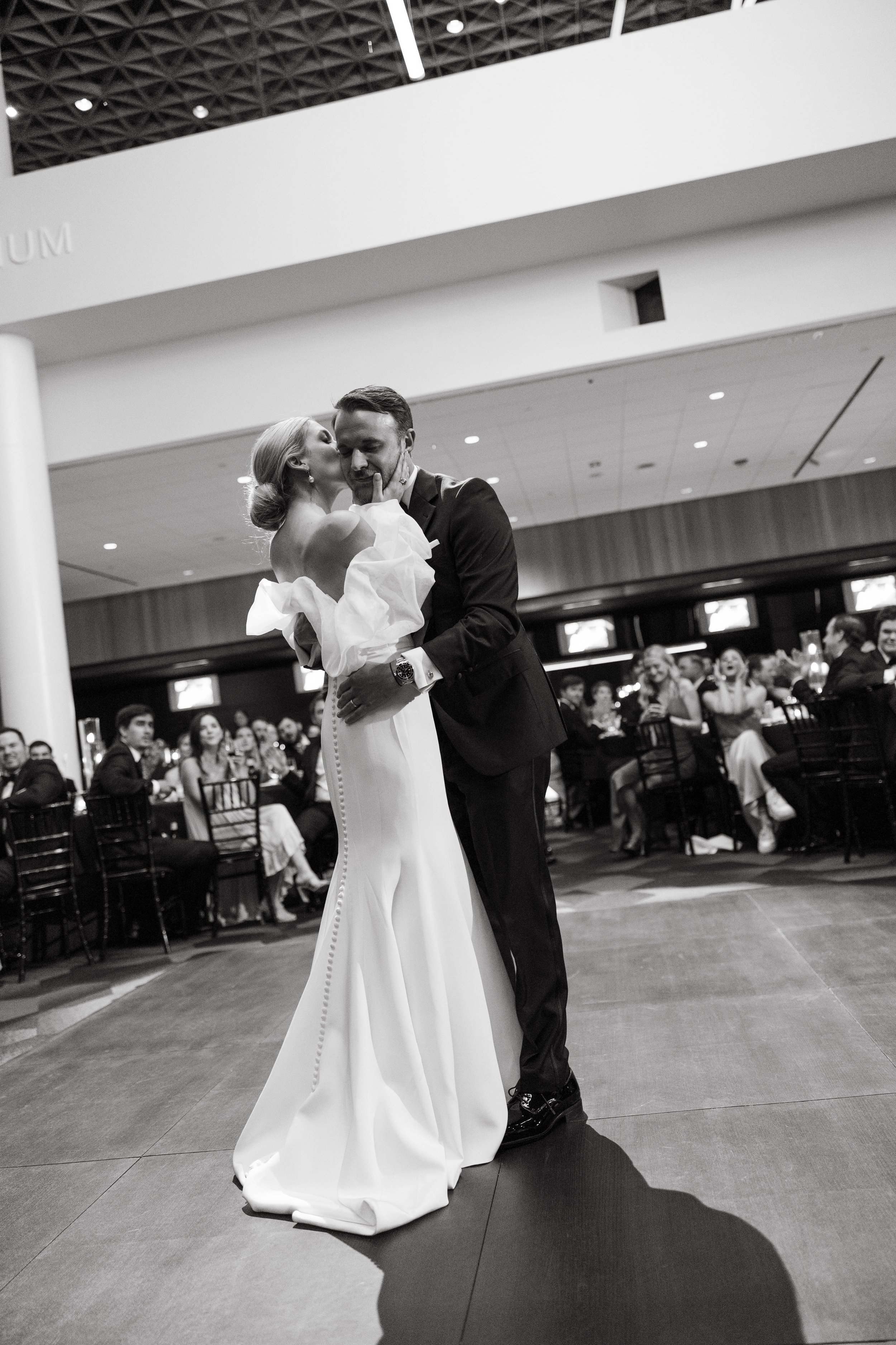 Bride and groom dancing in a formal setting, surrounded by seated guests