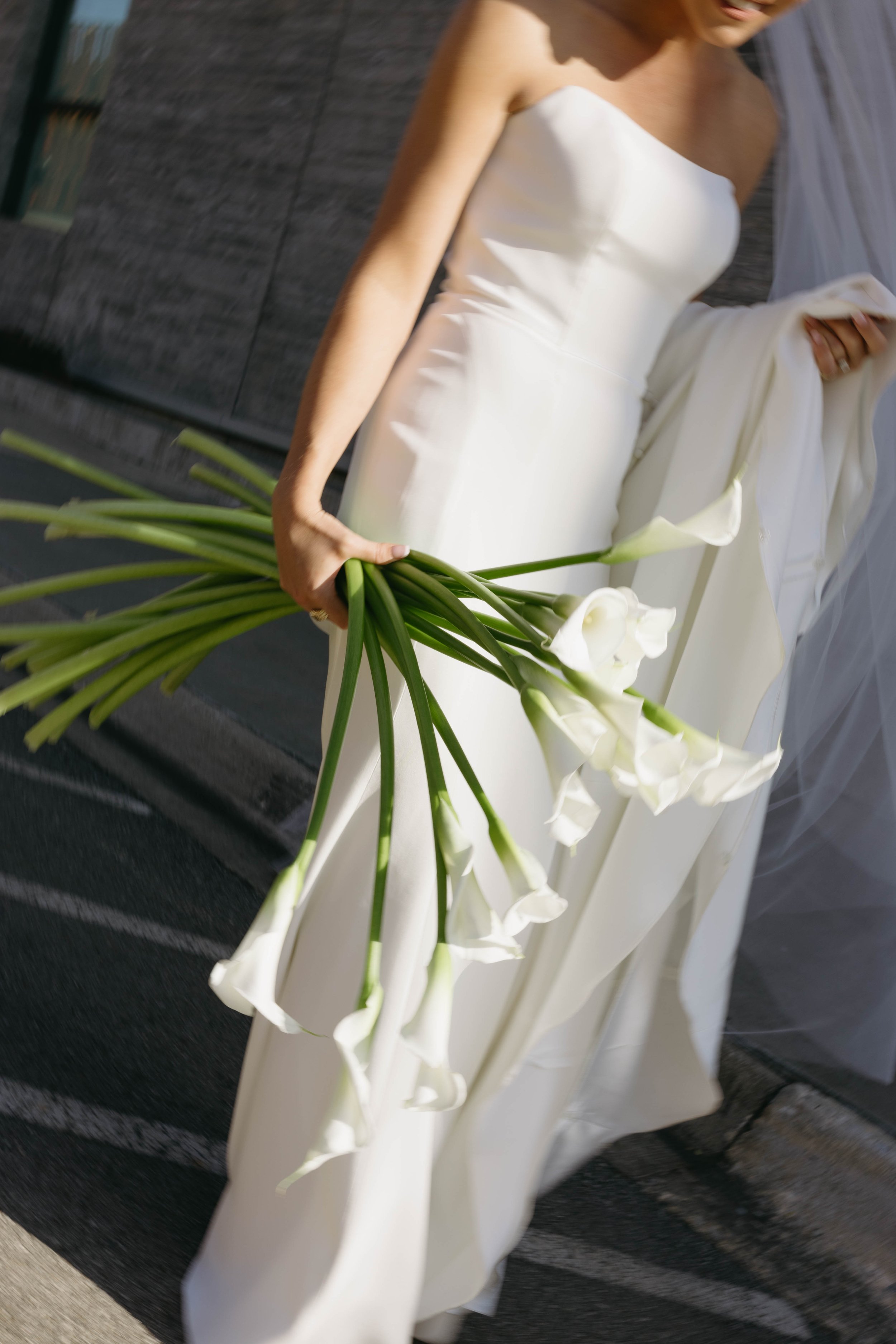 Bride in a white dress holding a bouquet of calla lilies outdoors.