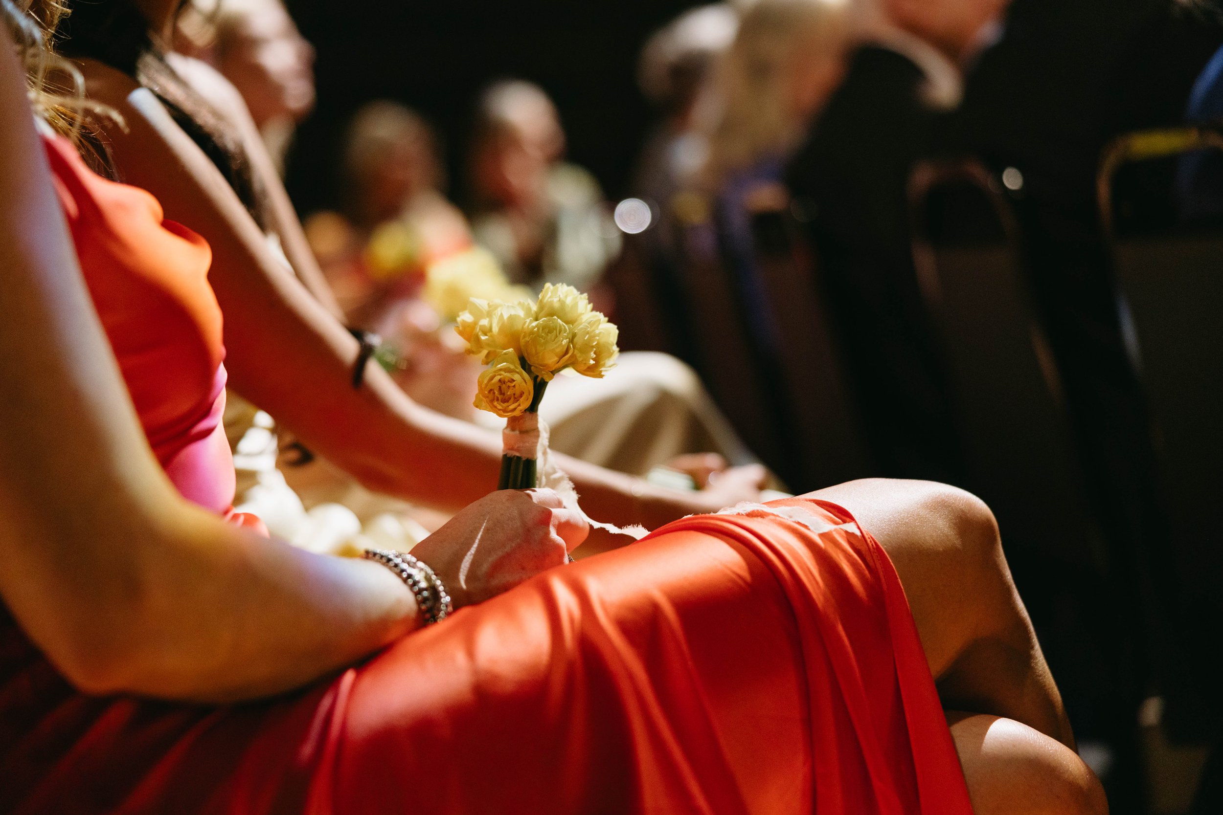 Close-up of a seated woman in a red dress holding a bouquet of yellow flowers during an event.