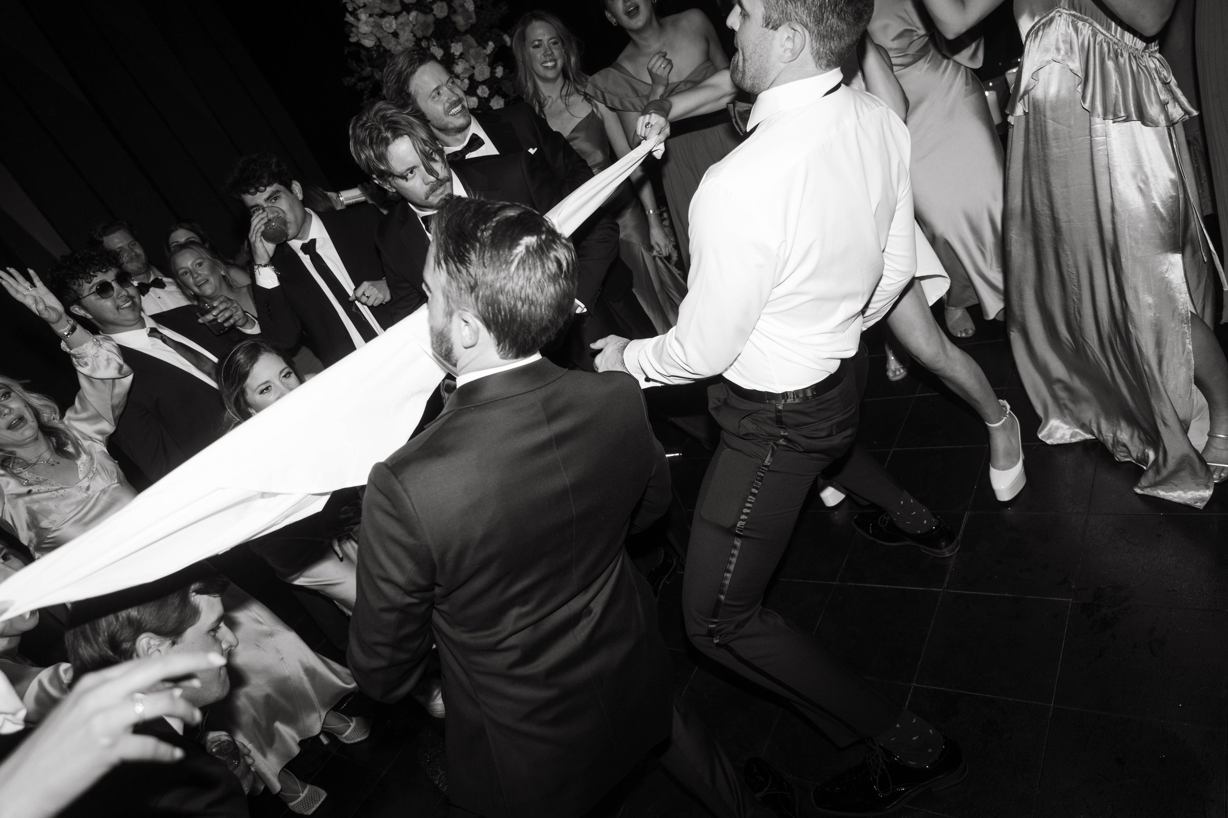 Group of people dancing and playing with a cloth at a party, wearing formal attire in black and white photo.