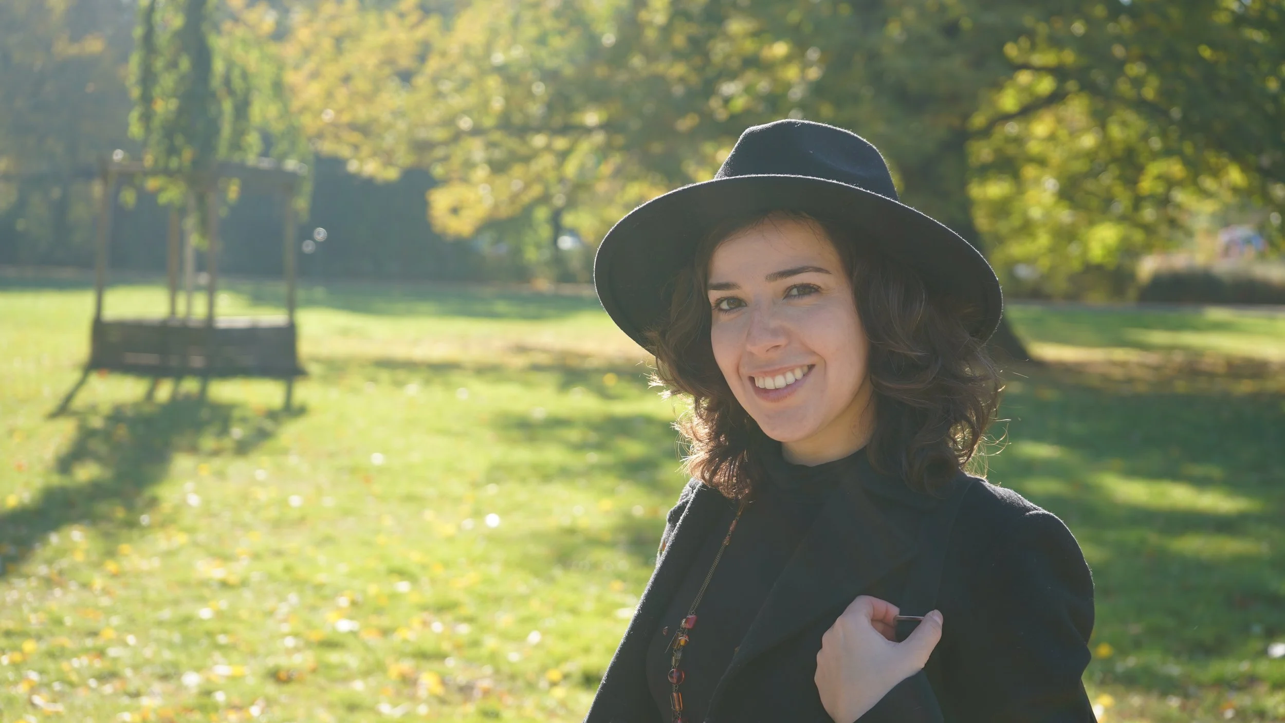 Portrait of Mariana Luna wearing a wool hat and black coat in a natural background with grass and trees