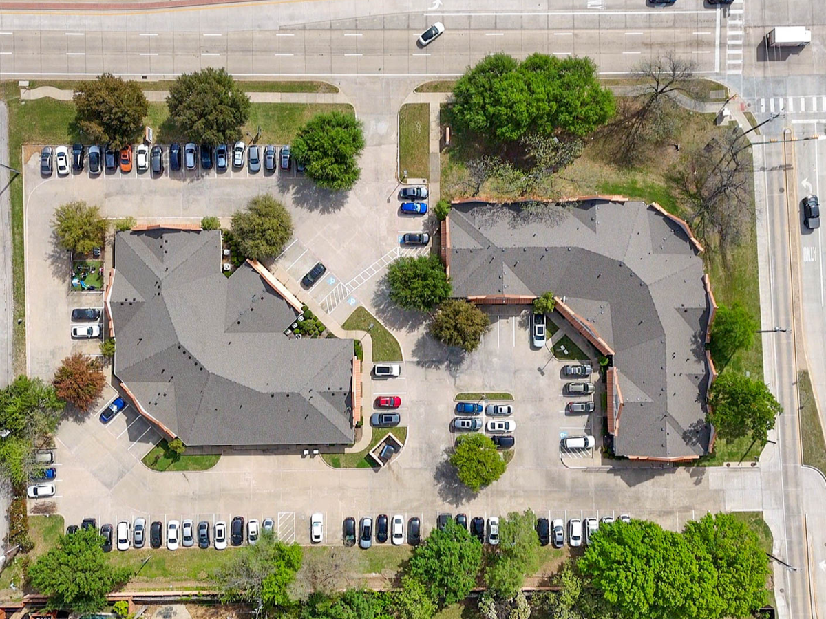 An aerial view of a residential apartment complex or office buildings surrounded by parking lots, green trees, and streets.