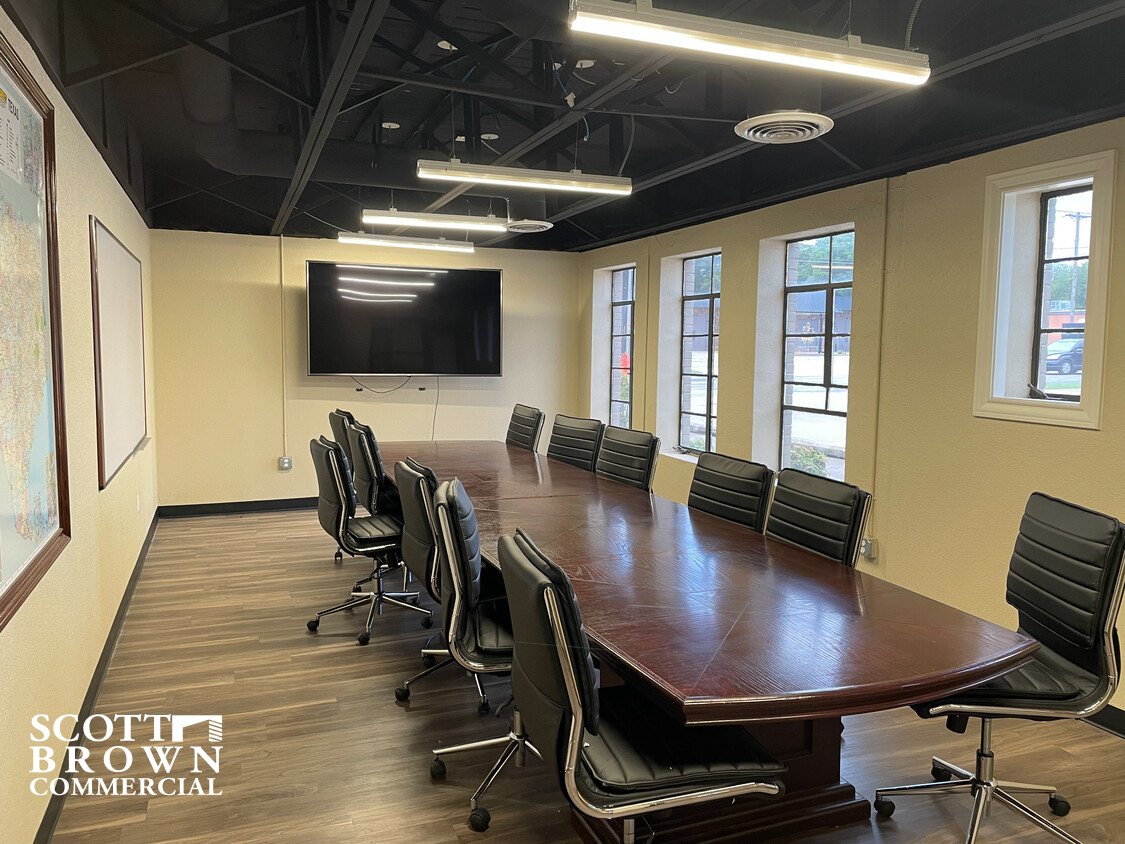  a meeting room within 419 S Elm Street with a long table and a tv mounted on the far wall with windows along the right wall 