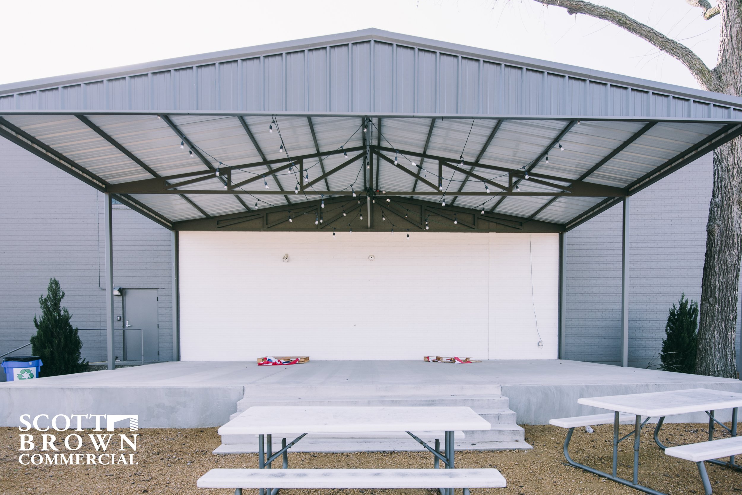  an outdoor concrete stage with picnic tables and tin roof 