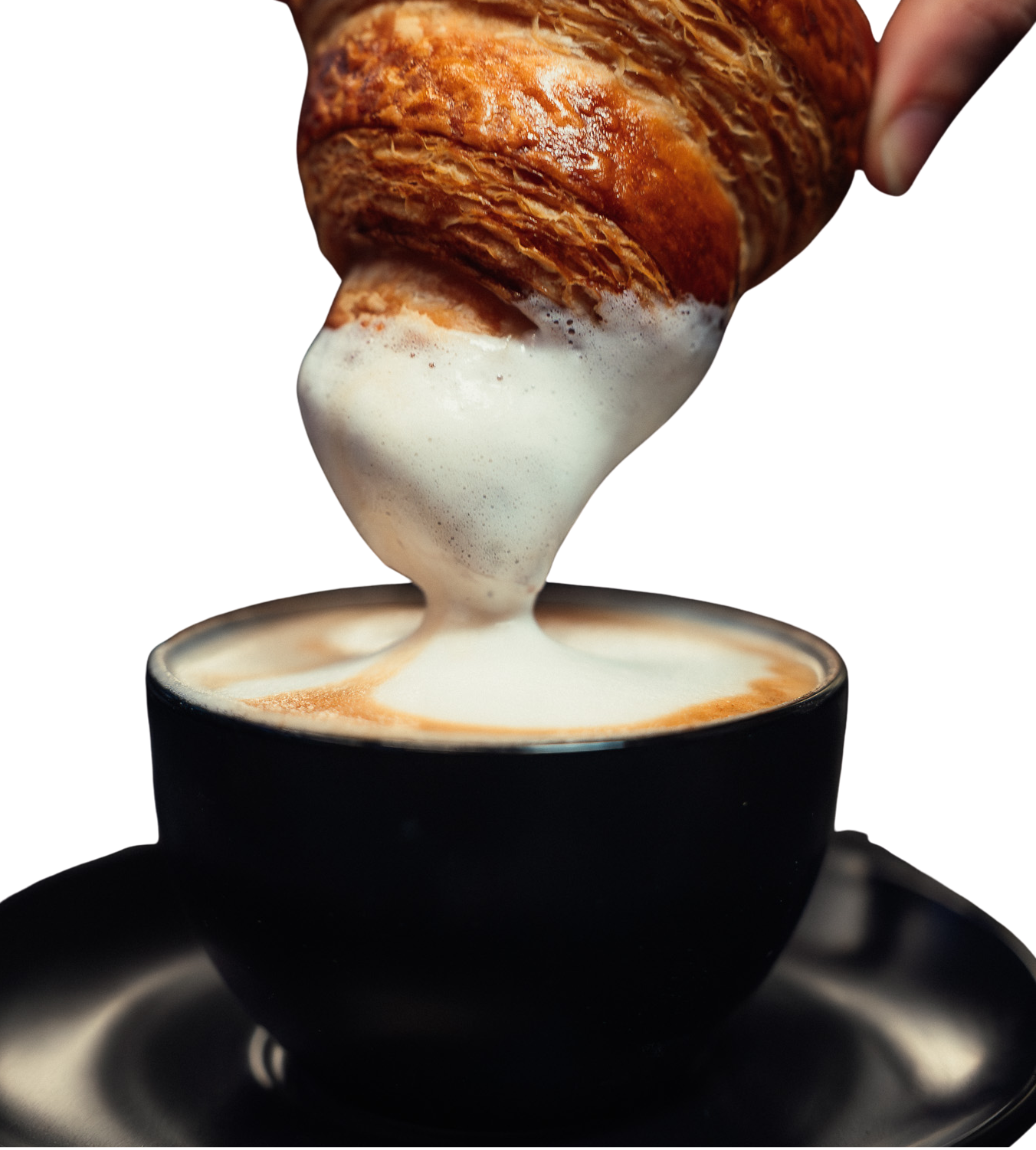 A croissant being dipped into a cup of frothy, creamy coffee in a black cup.