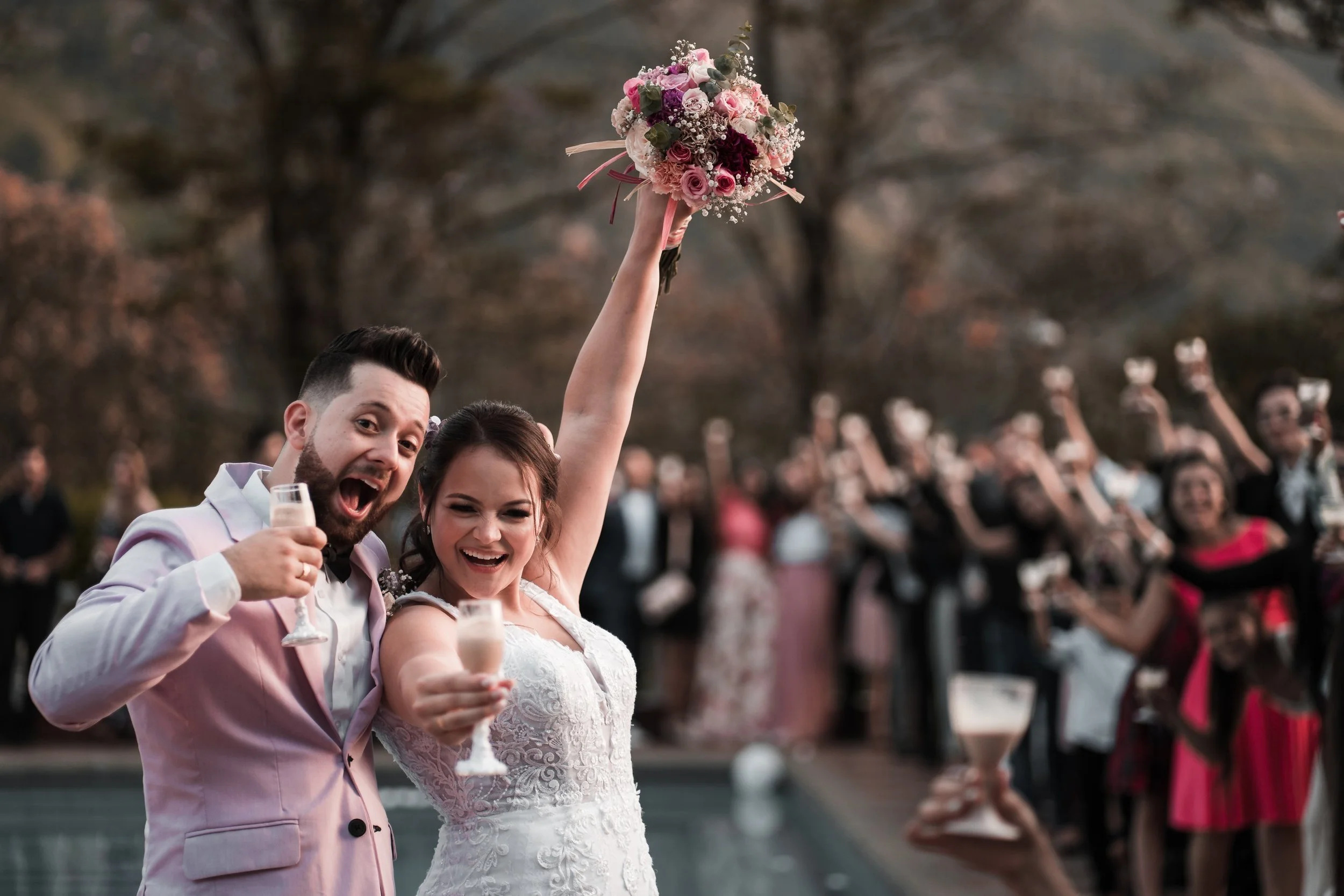 Arman and Sophie celebrating at their wedding, holding drinks and raising a bouquet