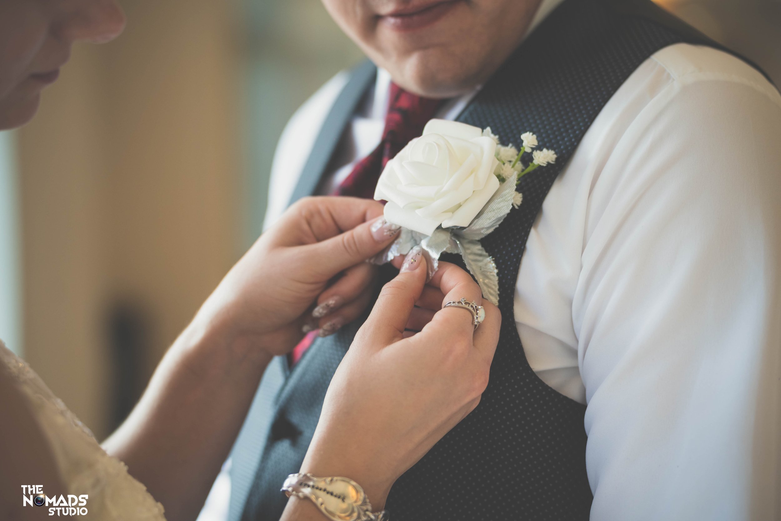 Close-up of a woman pinning a white rose boutonniere onto a man’s dark vest during a wedding ceremony.