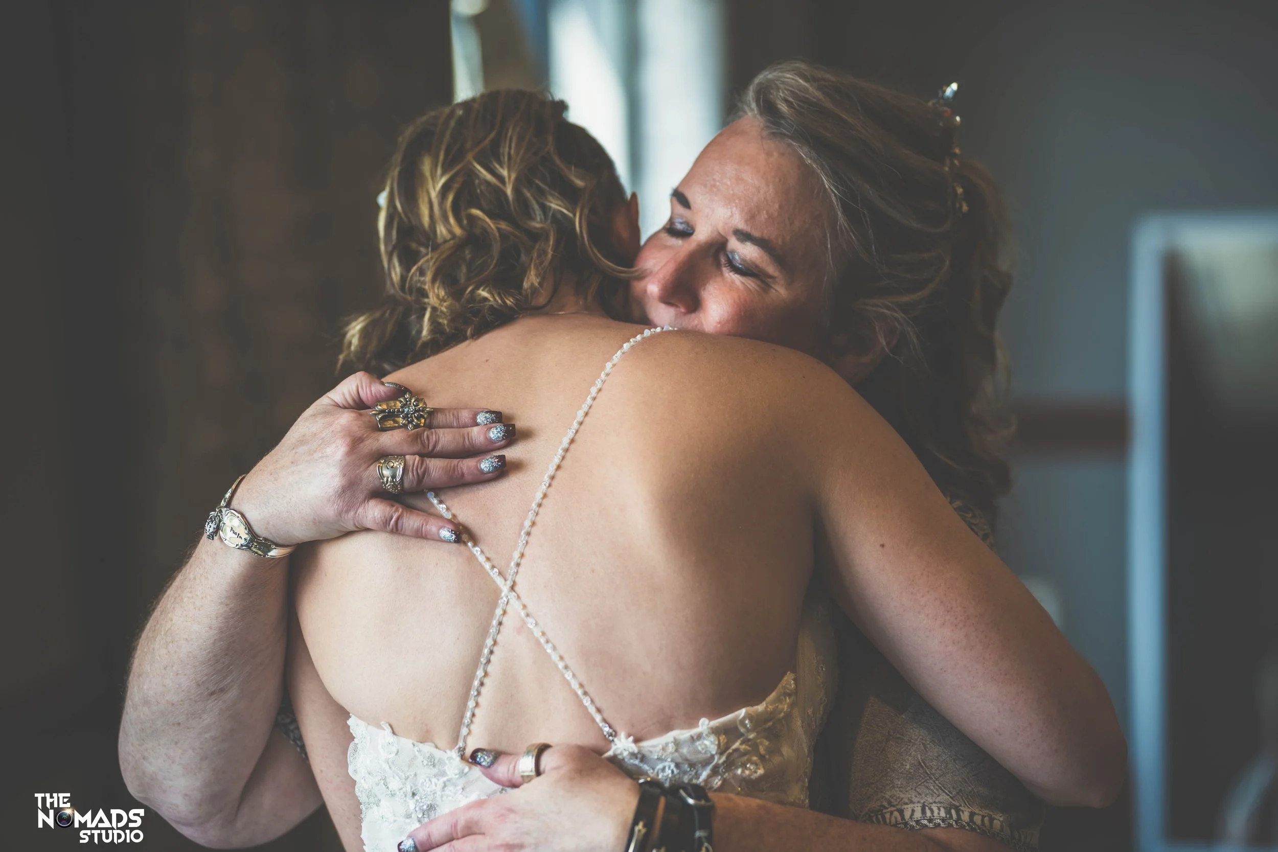 Two women hugging warmly indoors, one woman with curly hair and the other with straight hair, both with visible smiles and affection.