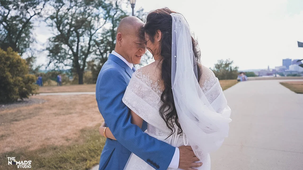 A bride and groom embrace with their foreheads touching outdoors during a wedding photoshoot.