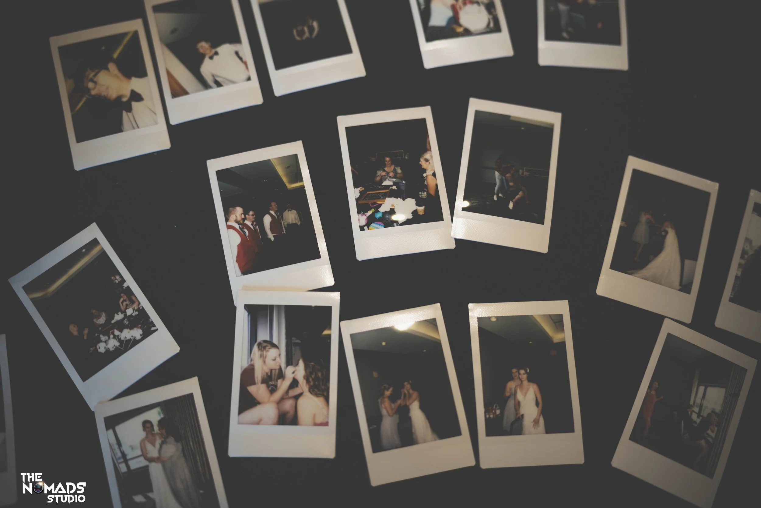A collection of printed photographs scattered on a dark surface, featuring various moments of people at a formal event or wedding, including couples, groups, and individuals posing or interacting.