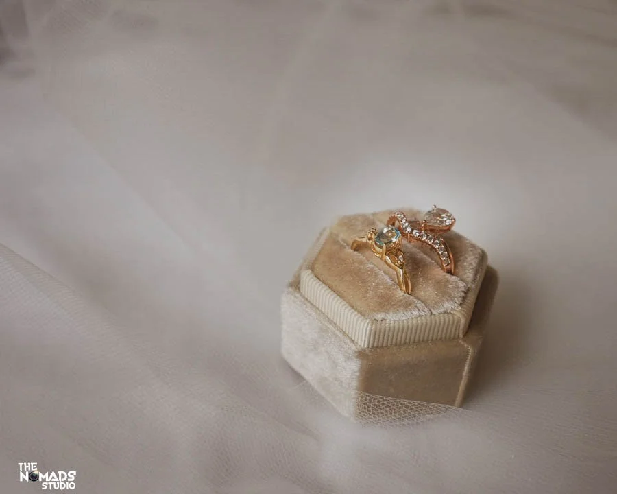 Two gold rings with gemstones on a beige velvet ring box