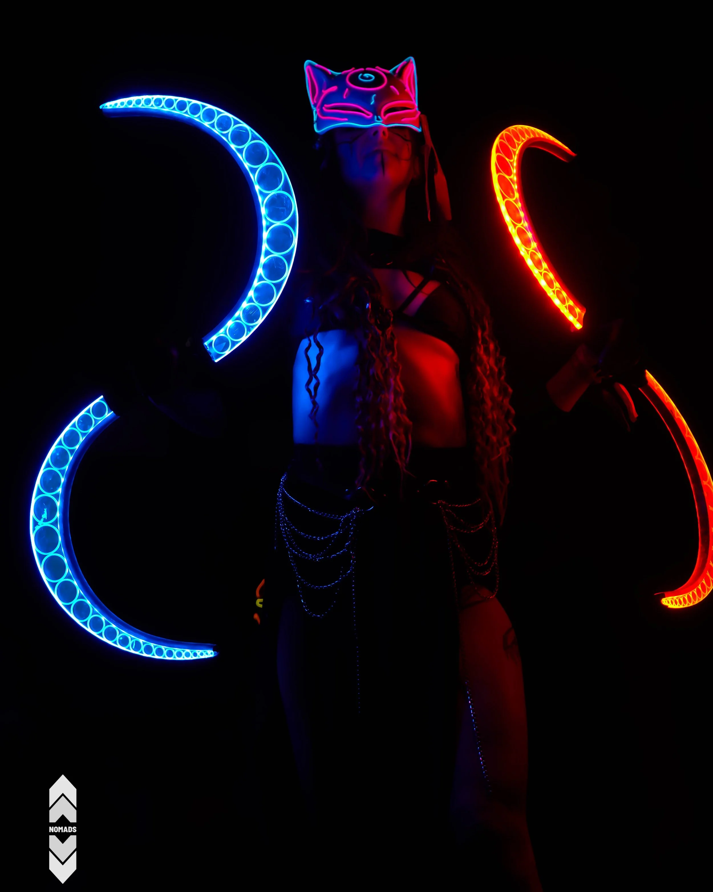 Person wearing glow-in-the-dark cat mask and black lingerie, surrounded by illuminated neon crescent shapes in blue and red lights against a dark background.
