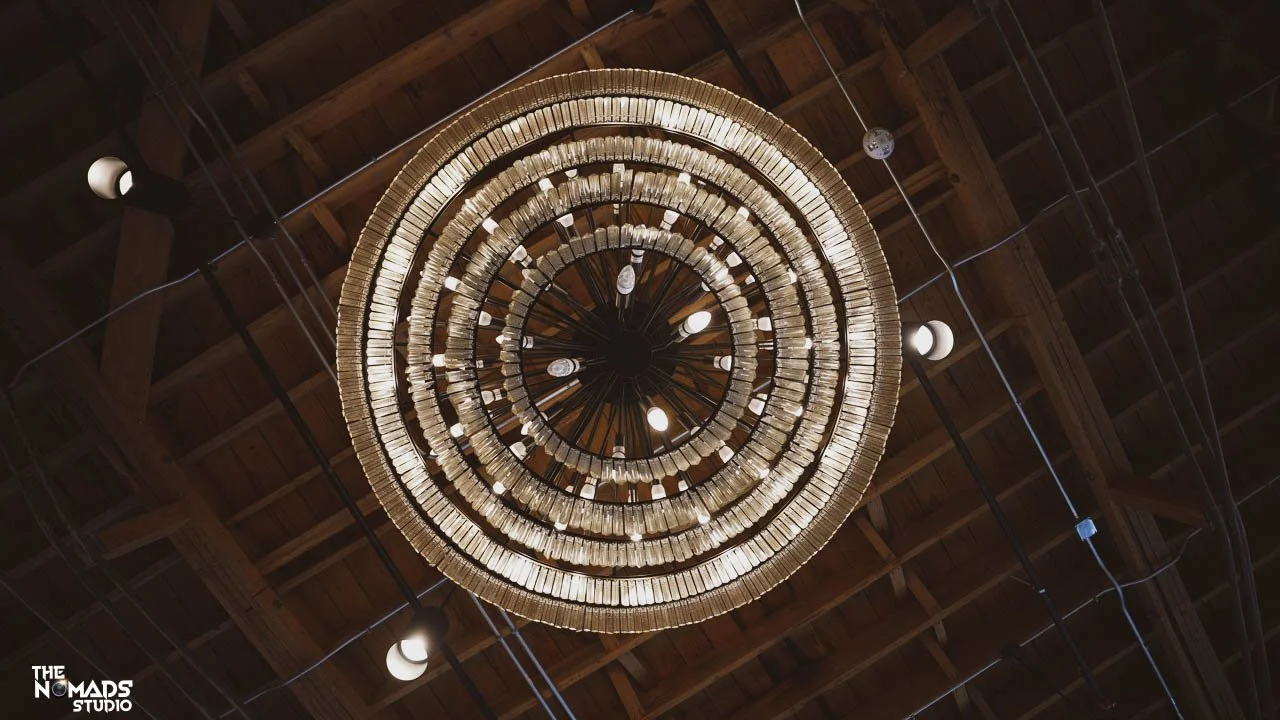A circular chandelier made of numerous books hanging from a wooden ceiling with visible beams and track lights.