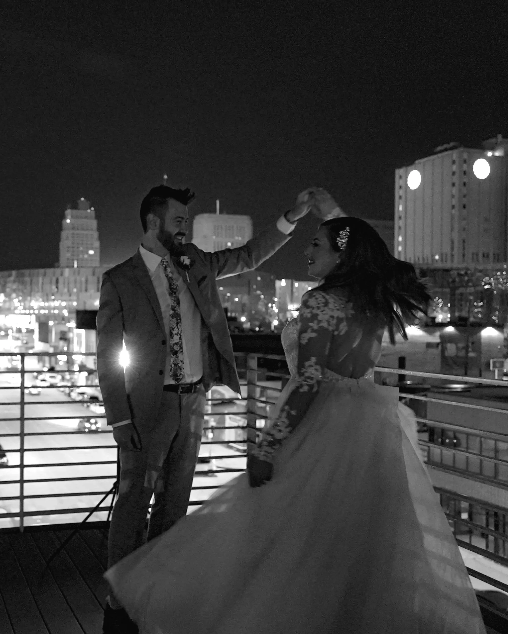 Newlyweds dancing on a rooftop at night with the city skyline behind them