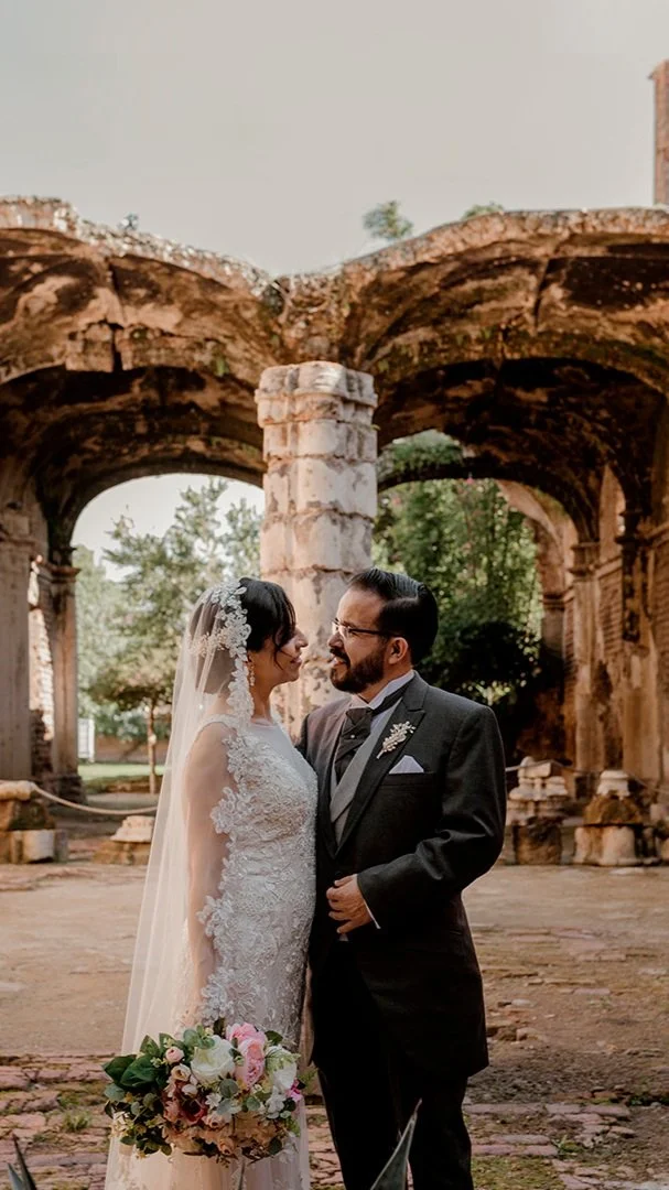 Bride and groom standing together beneath historic stone arches
