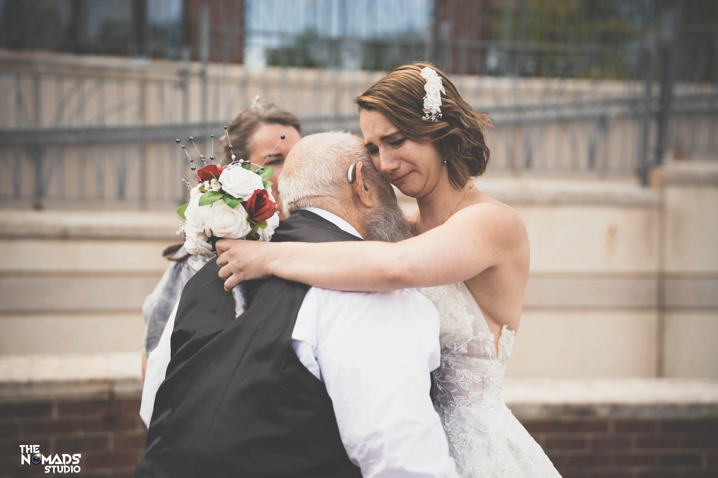 A woman in a wedding dress hugging an elderly man wearing a black suit during a wedding celebration outside.