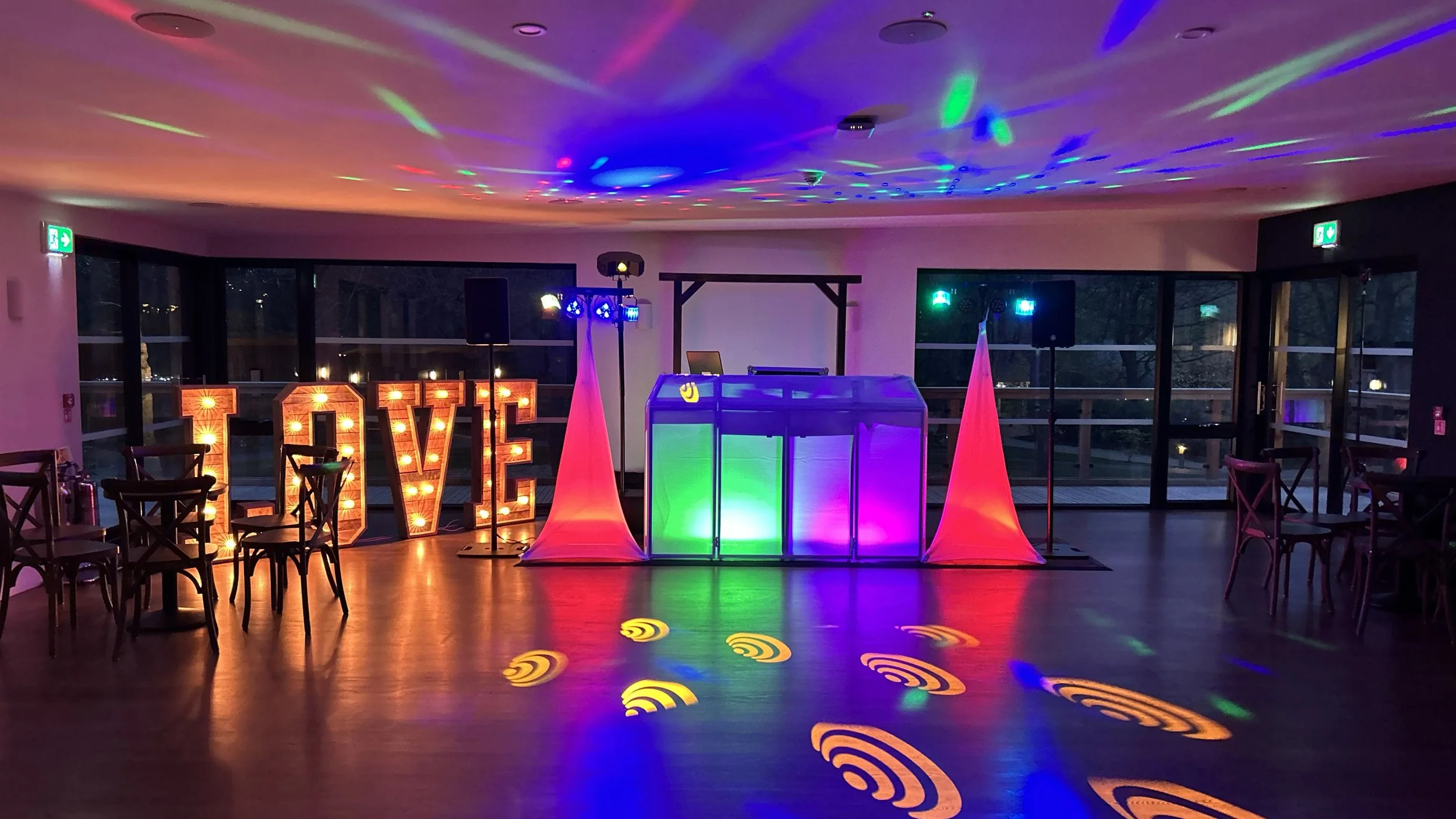 Interior of a room set up for a party, featuring colorful disco lights, speakers, and abstract wall art.