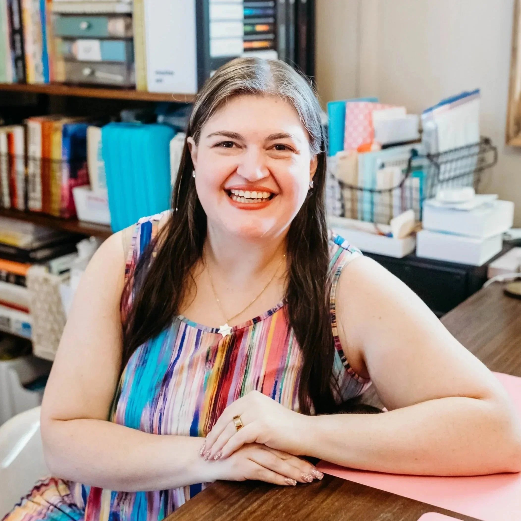 Smiling woman wearing a striped dress with a colorful bookshelf behind her