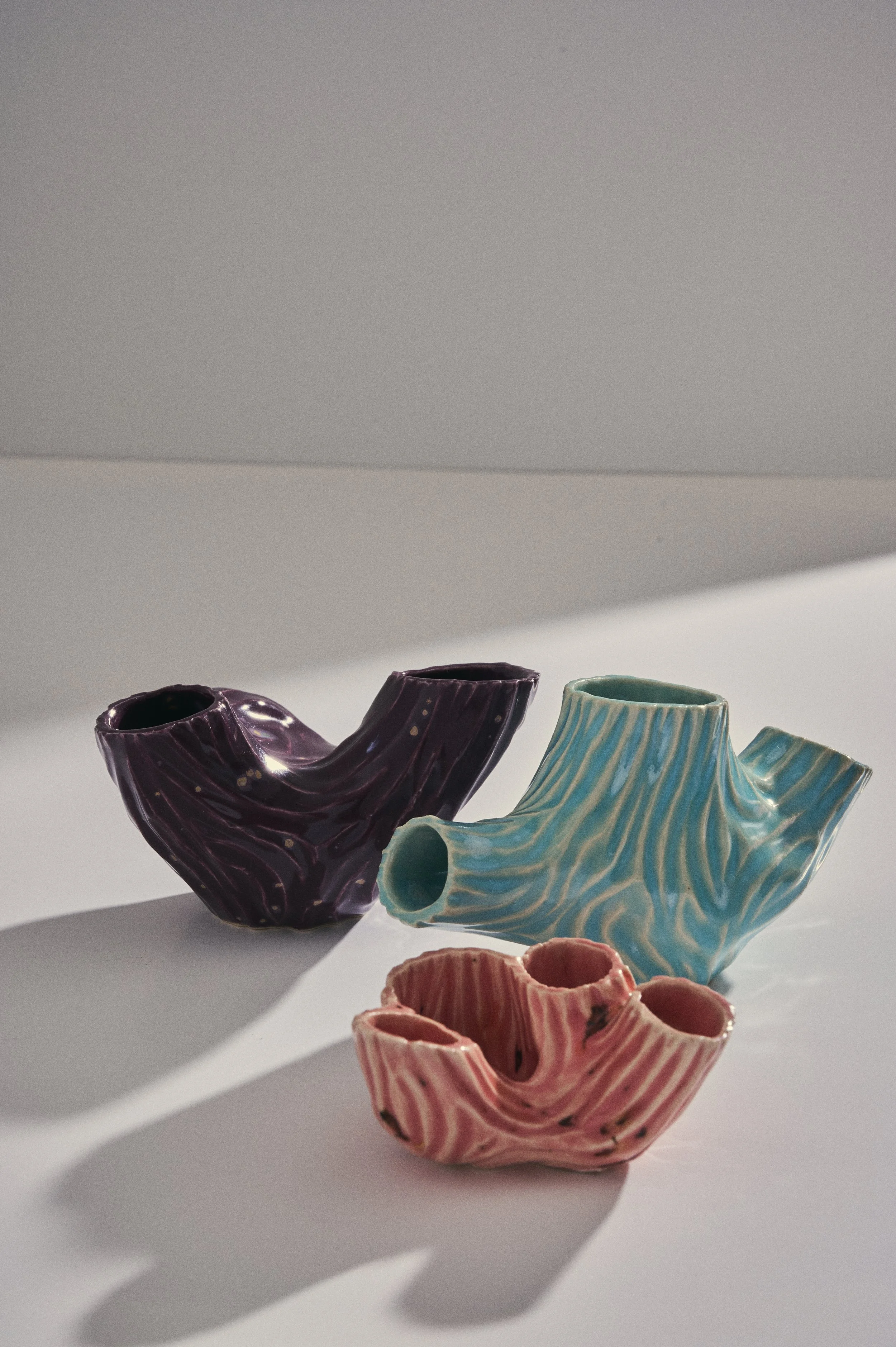 Colorful ceramic Alien scultures in purple, blue, and pink with artistic patterns, arranged on a white surface with shadows cast by natural light