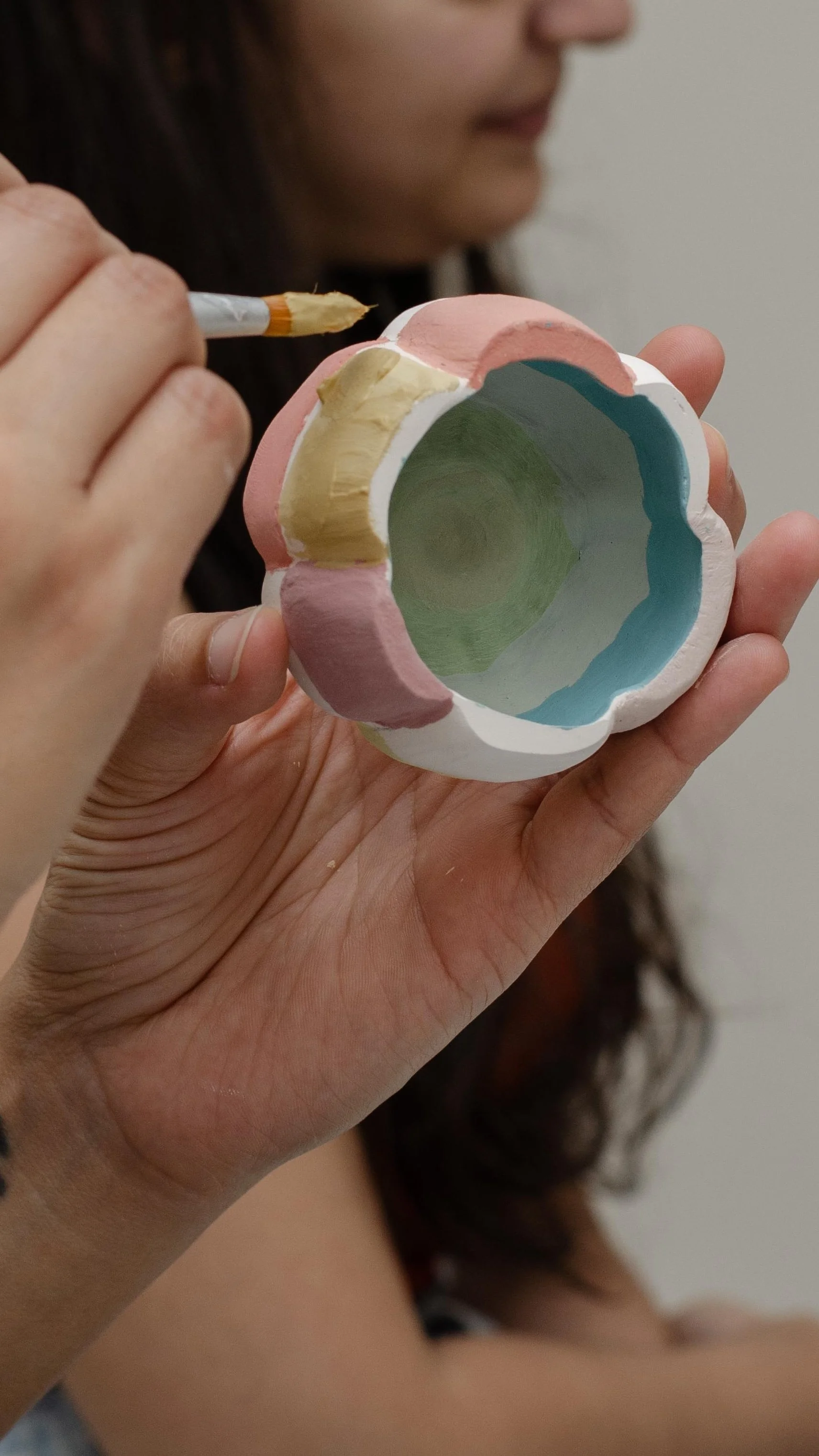 A person is holding a colorful, hand-painted ceramic bowl and using a small brush to add details to it.
