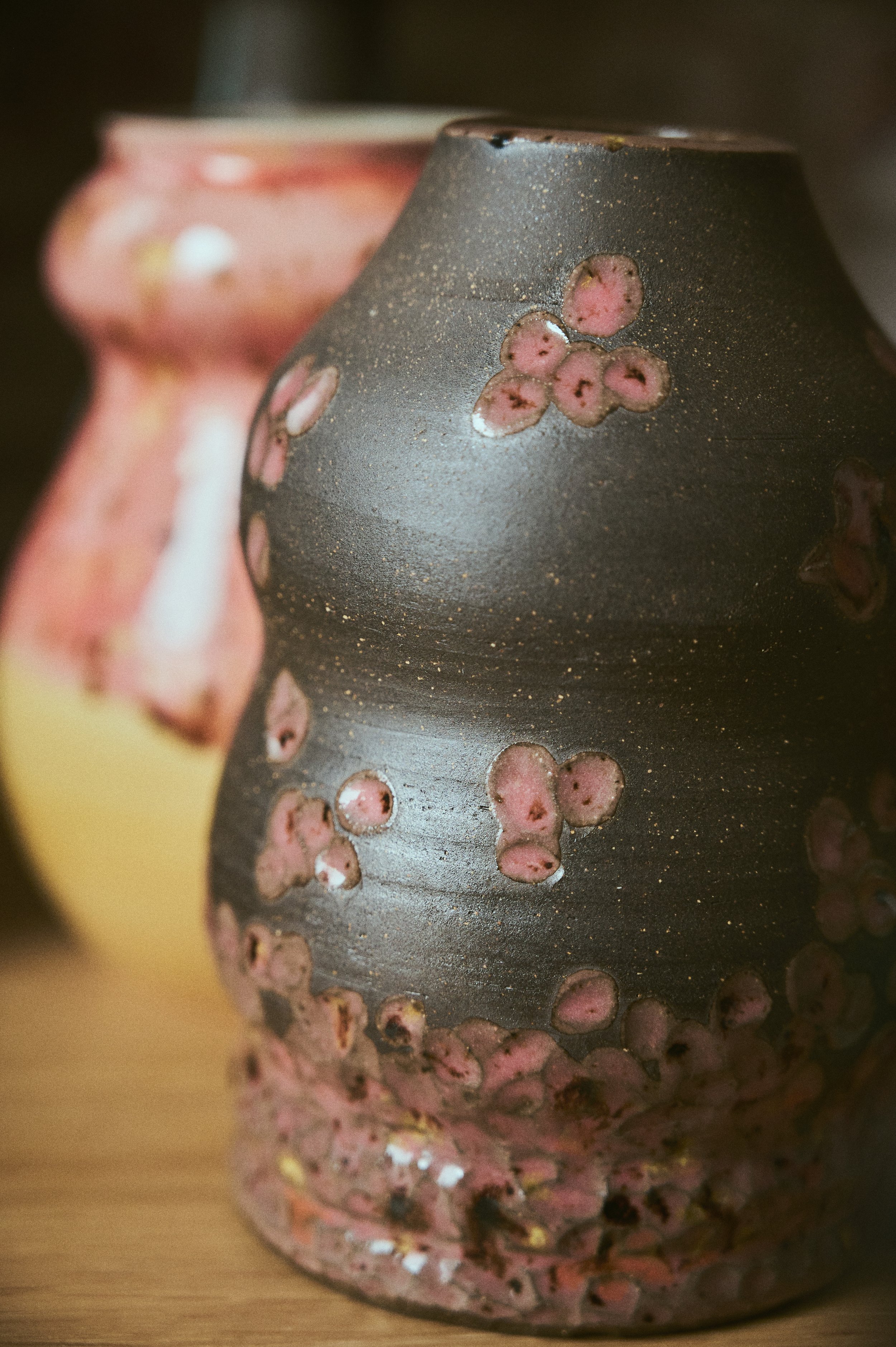 Close-up of a ceramic vase with pink floral patterns, placed on a wooden surface.