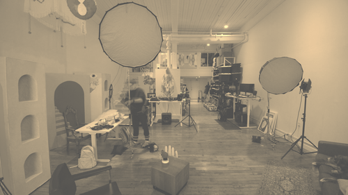 A photography and filming studio with two large softbox lights, a table with various objects, chairs, and industrial shelves on the wall, creating an artsy workspace. This is ZERO*NDA Montreal studio.