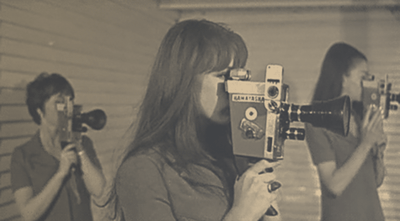 Three women using vintage film cameras to take photographs in an indoor setting.