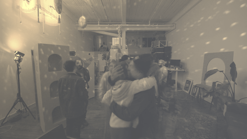 Friends hugging at a social gathering with several other people in a room decorated with disco lights and artwork. This is an event at ZERO*NDA Montreal studio.