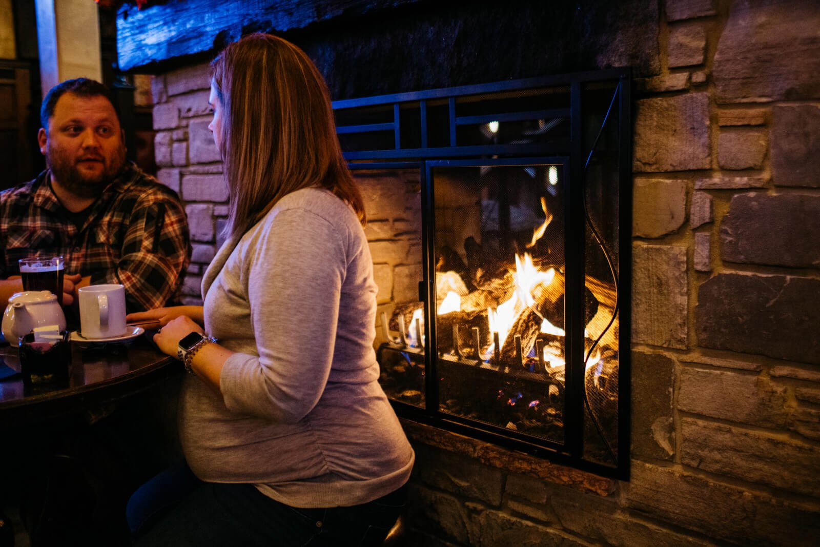  Couple enjoying dinner by a fireplace for a maternity photoshoot 