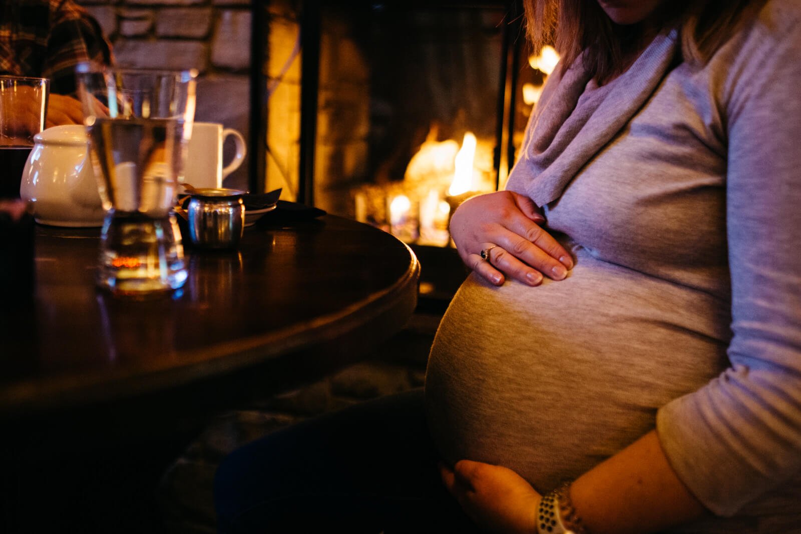  Pregnant woman holding her belly by a fireplace 