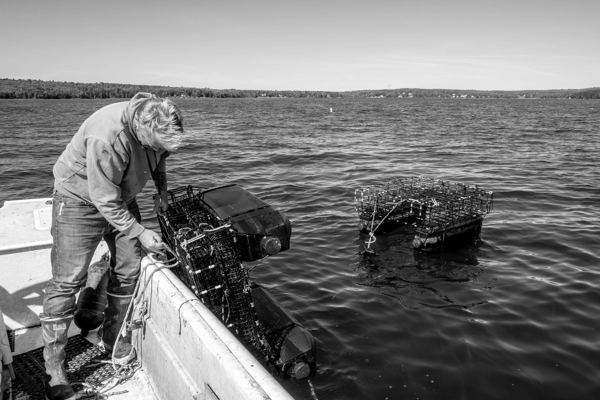 Graham Platner  on a boat handling traps or cages in the water and forested shoreline in the background. Photo by Nick Gervin.