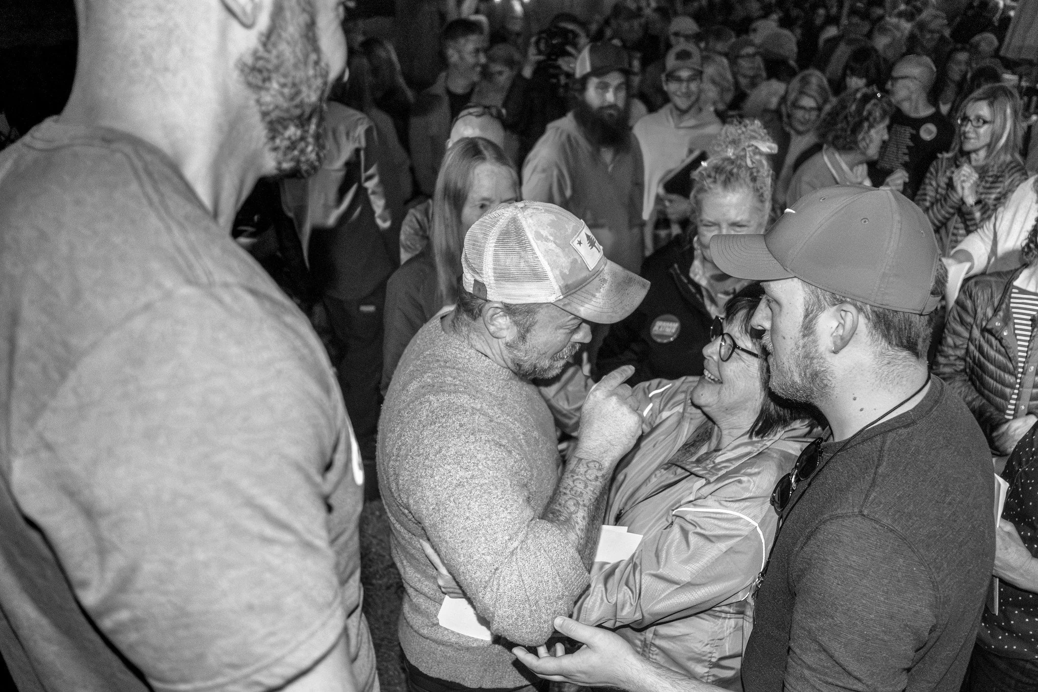 A large group of people gathered, interacting warmly. In the foreground, a woman with glasses and Graham Platner are engaged in a close conversation, smiling. Photo by Nick Gervin.