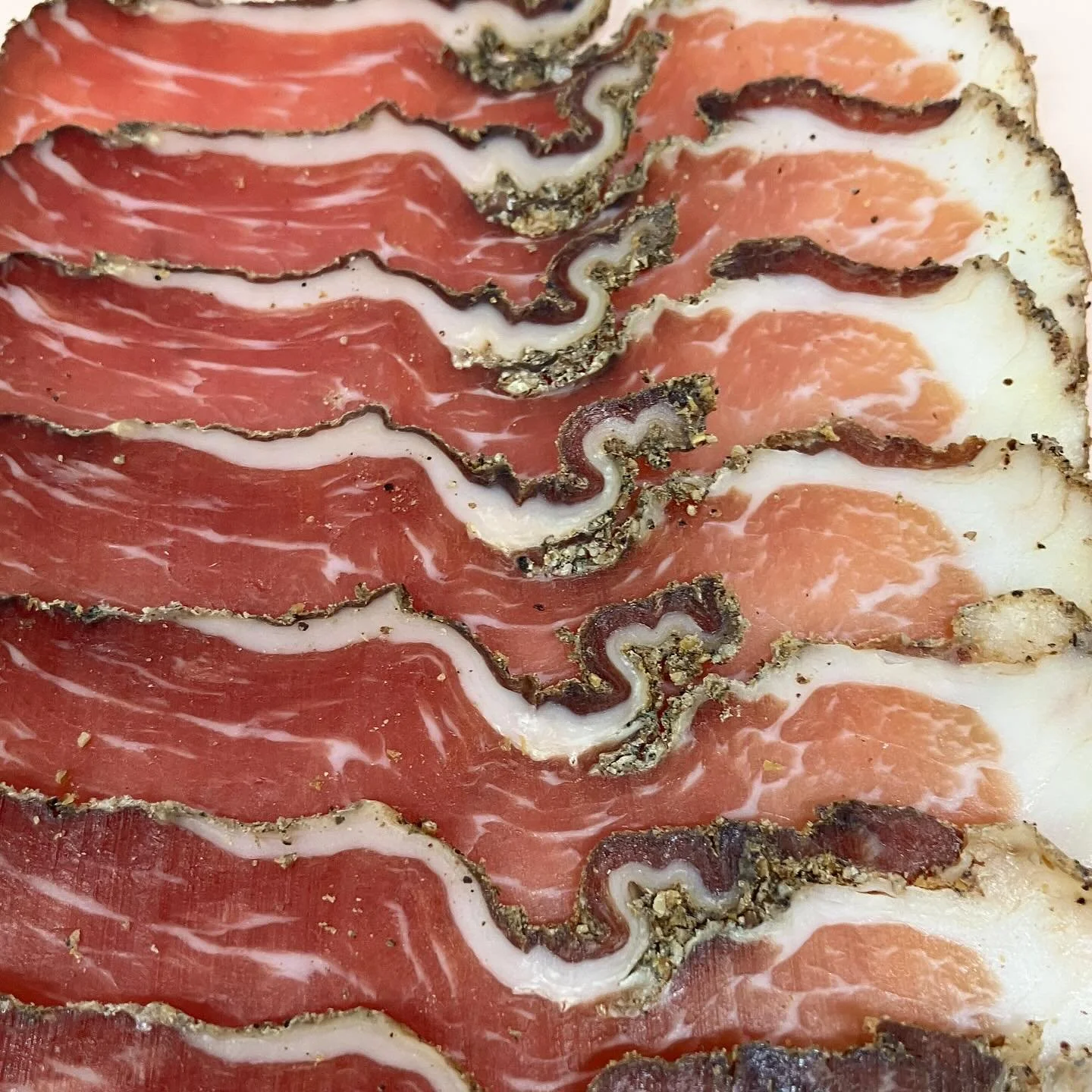 Close-up of sliced cured meats, including prosciutto and other charcuterie, with visible marbling and peppercorn crust.