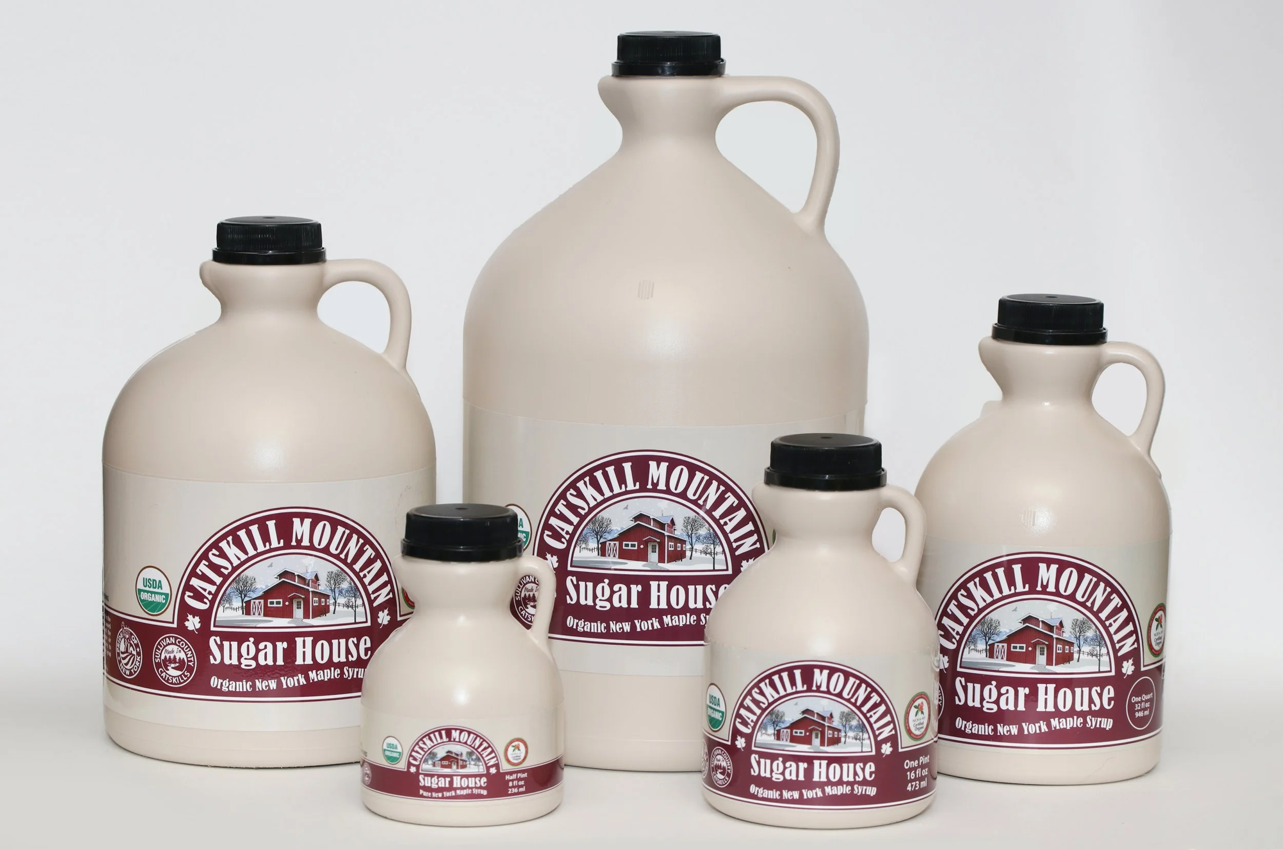 Six bottles of Catskill Mountain Sugar House organic New York maple syrup in various sizes against a plain background.