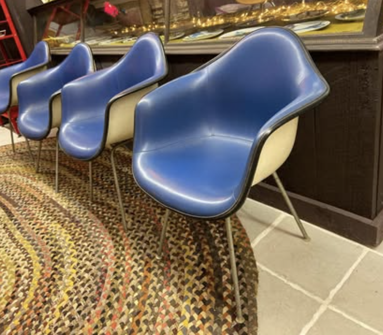 Three vintage blue chairs with metal legs arranged in a row on a colorful woven rug in an indoor space.