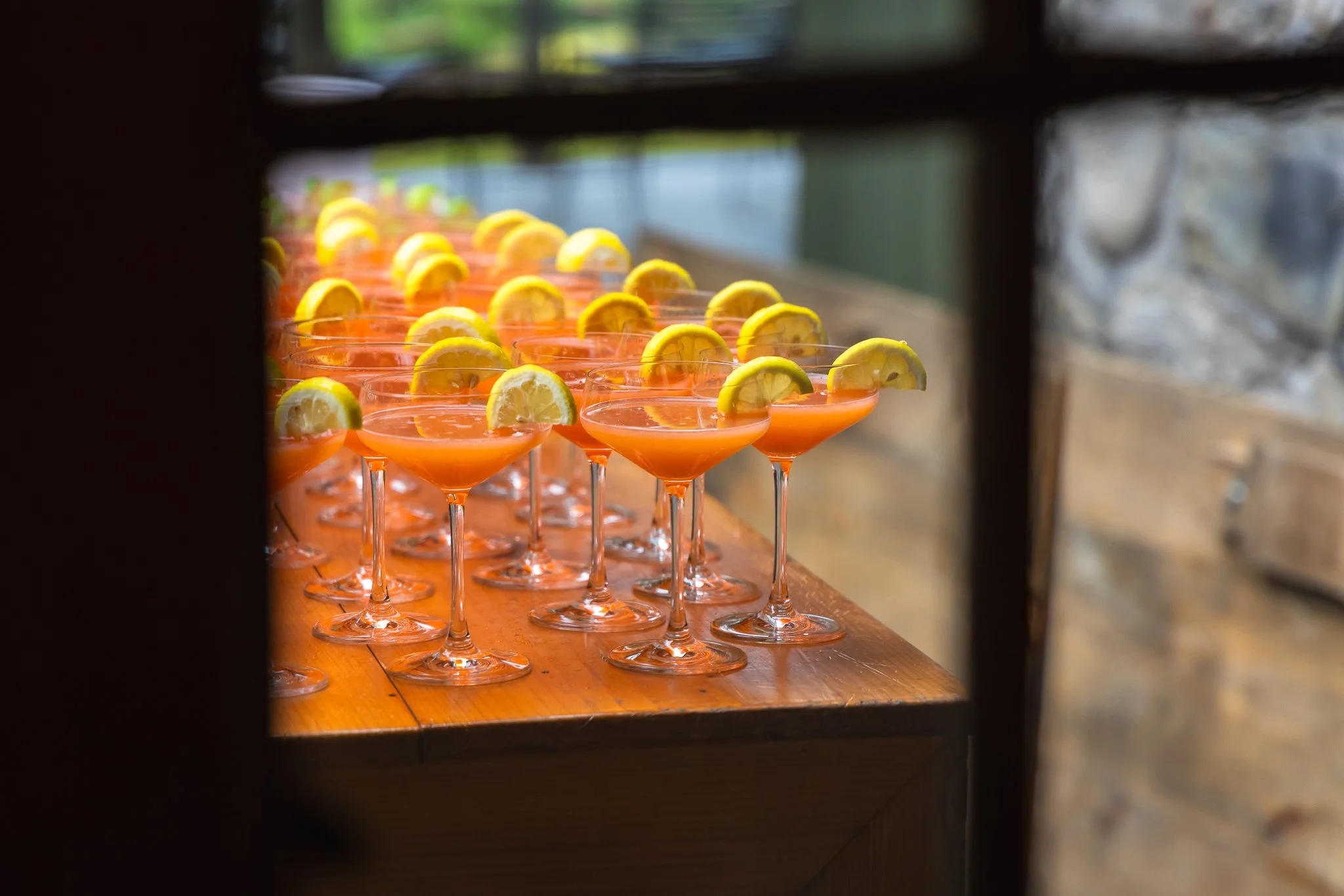 A row of pink cocktails garnished with lemon wedges on a wooden table.