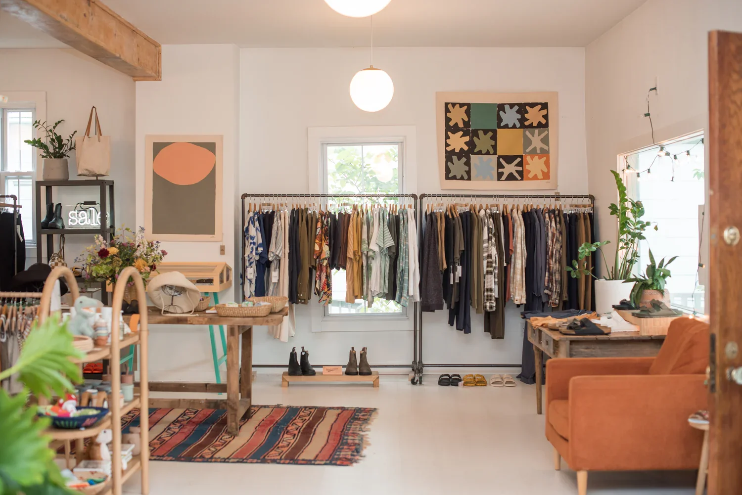Interior of a boutique clothing store with racks of clothes, indoor plants, artwork, and a sofa.