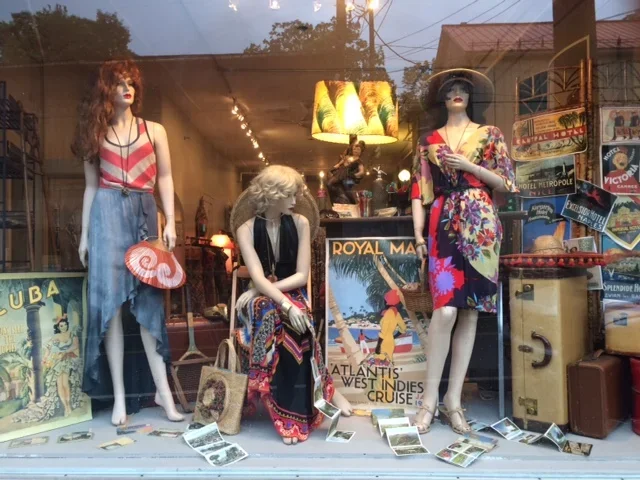 Display window with three mannequins dressed in vintage clothing, surrounded by travel posters and souvenirs.