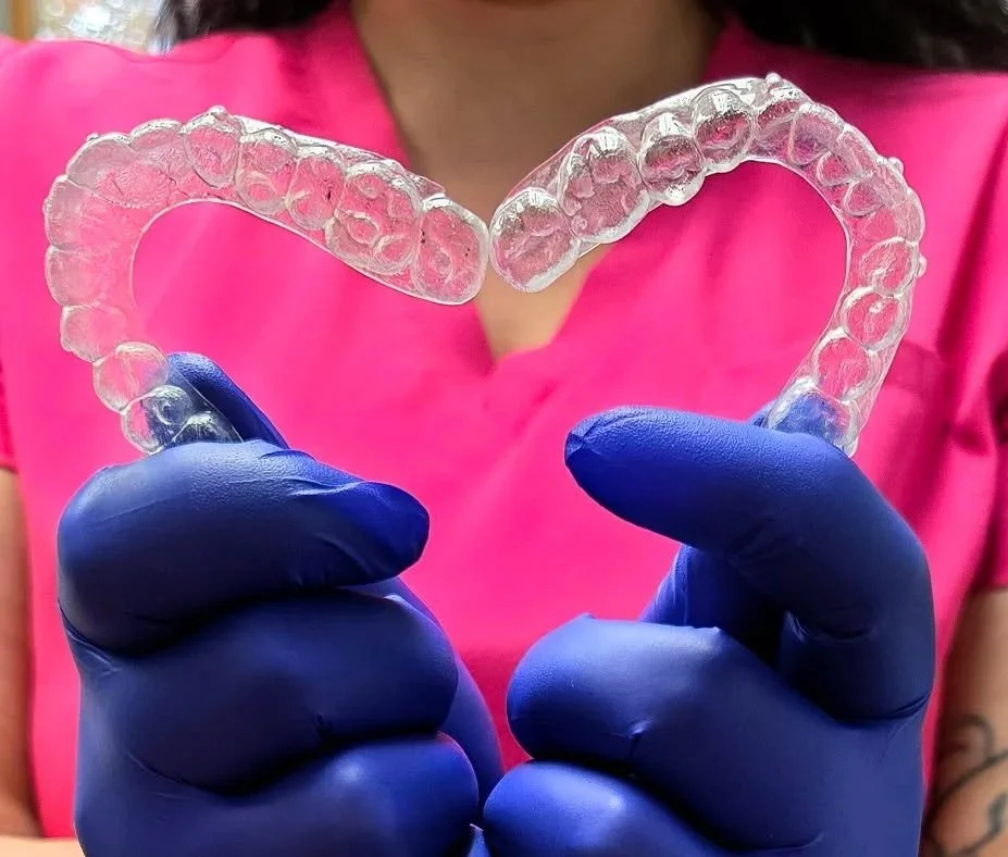A modern house with wooden exterior walls and a large glass window, set in a mountainous landscape with grassy foreground and rugged peaks in the background.
