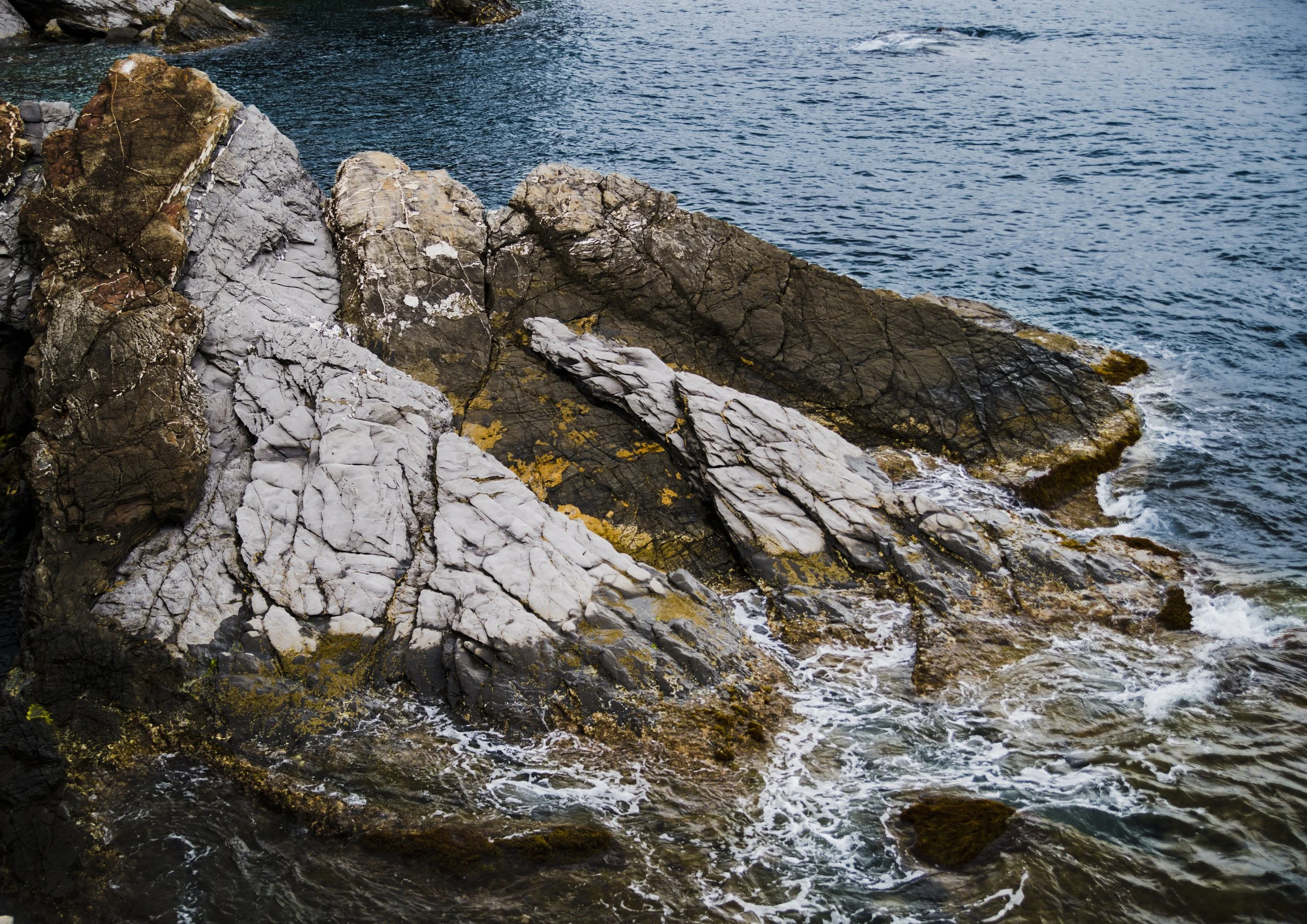 Rocks along the shoreline with ocean waves crashing against them.