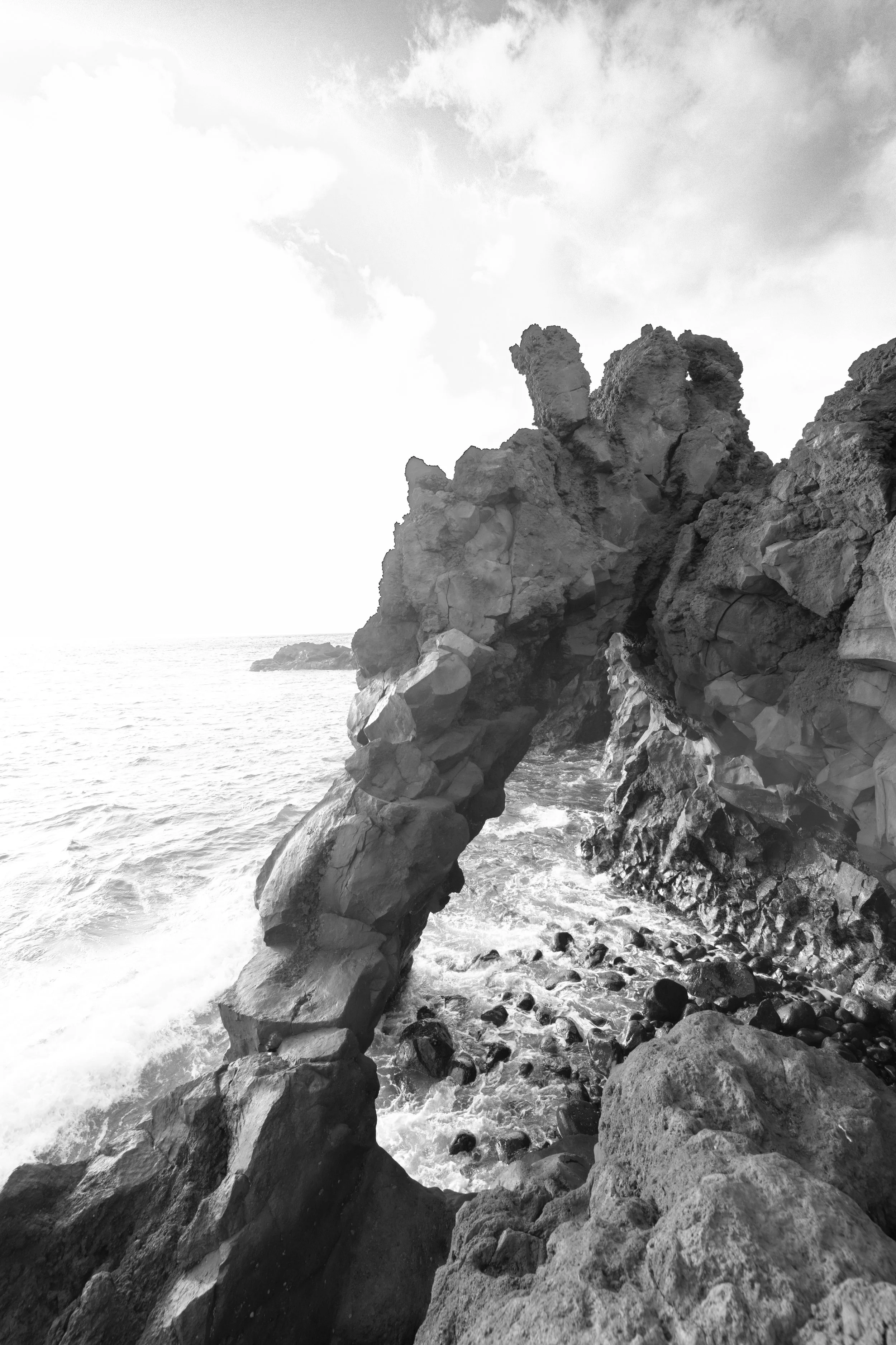 A black and white photo of a coastal landscape with large rock formations and the ocean waves crashing against the rocks.