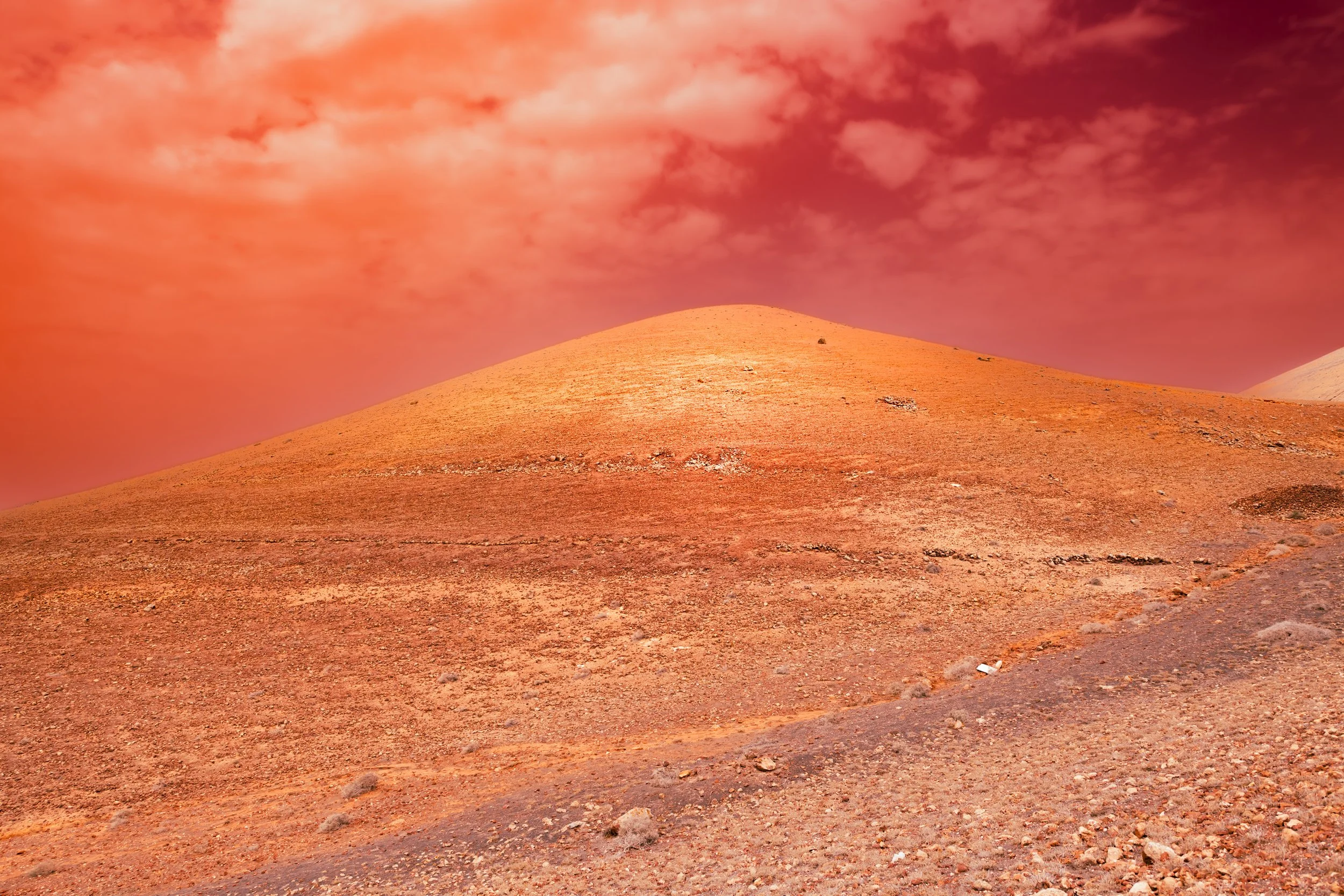A barren, rocky desert landscape with a reddish hue under a sky filled with pinkish clouds.