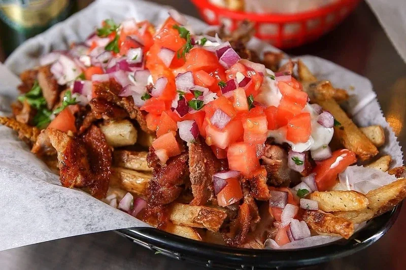 A plate of loaded fries topped with chopped tomatoes, onions, tzatziki, and cheese.