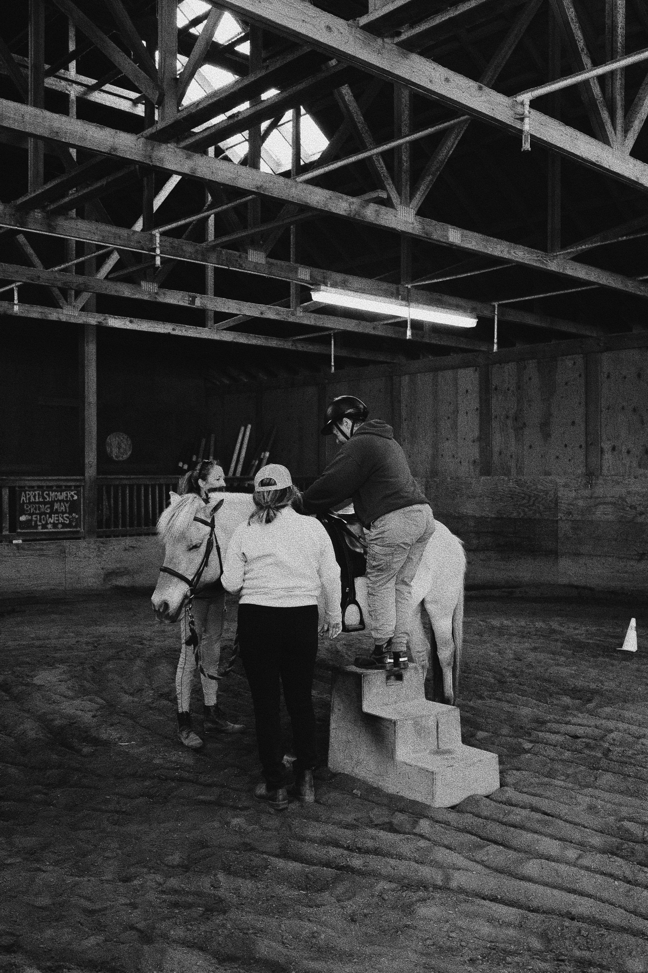 A person mouting a horse in an indoor arena with the help of other people