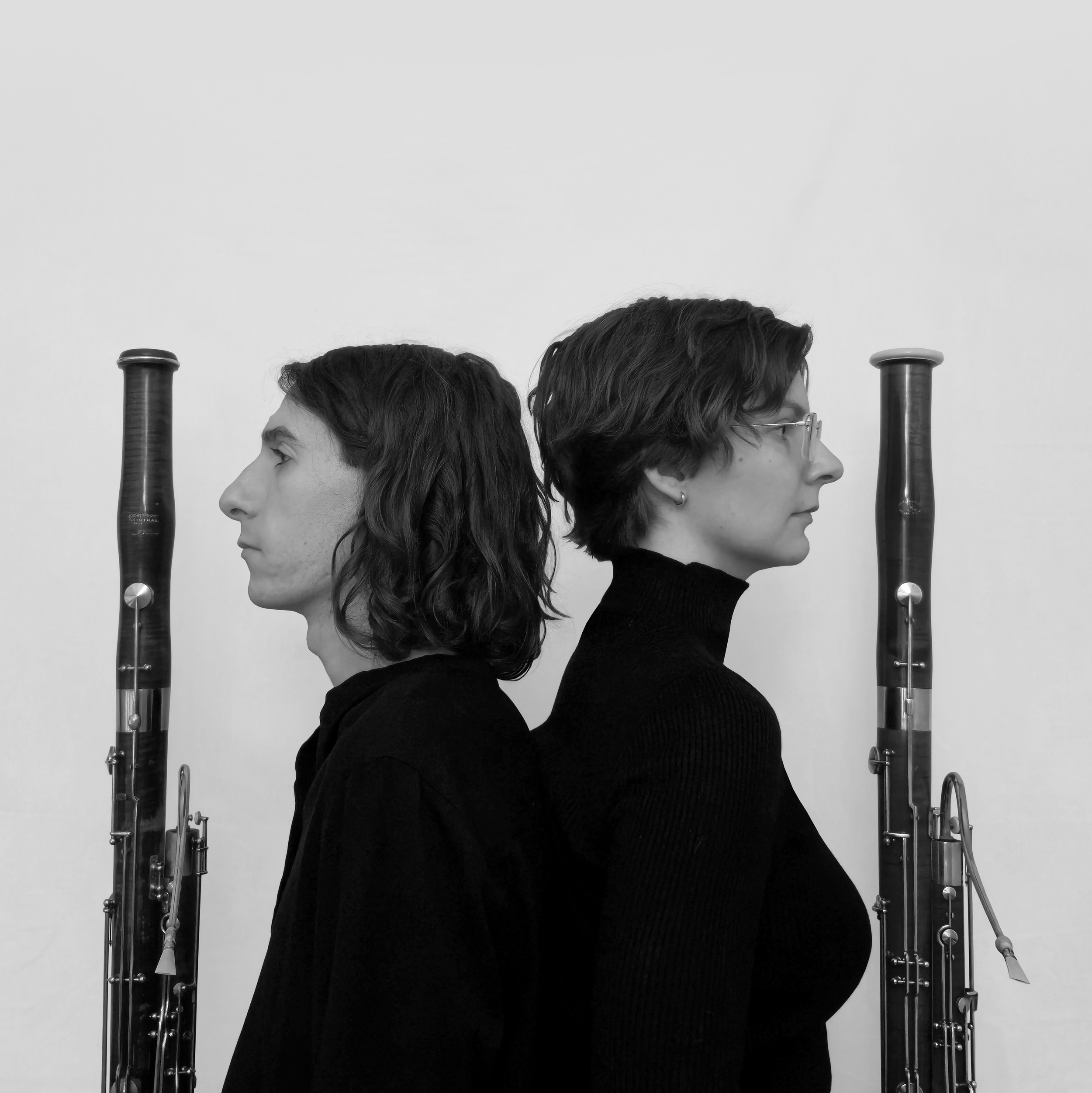 Bridge Bassoon Duo headshot in grayscale. Andy Sledge and Dana Brink in profile facing away from each other, bordered by the bells of their bassoons.