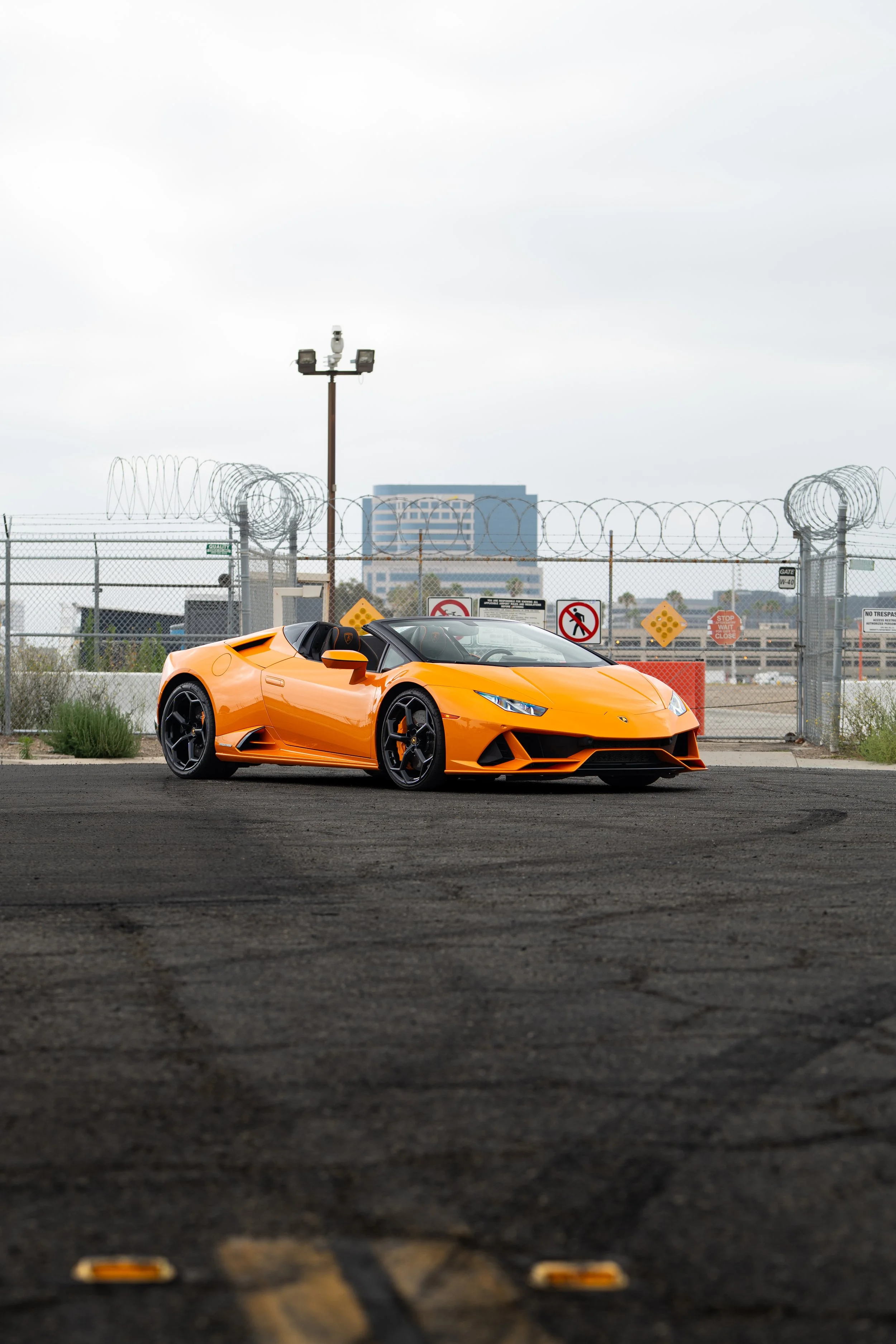 Orange Lamborghini convertible parked in front of a barbed-wire security fence